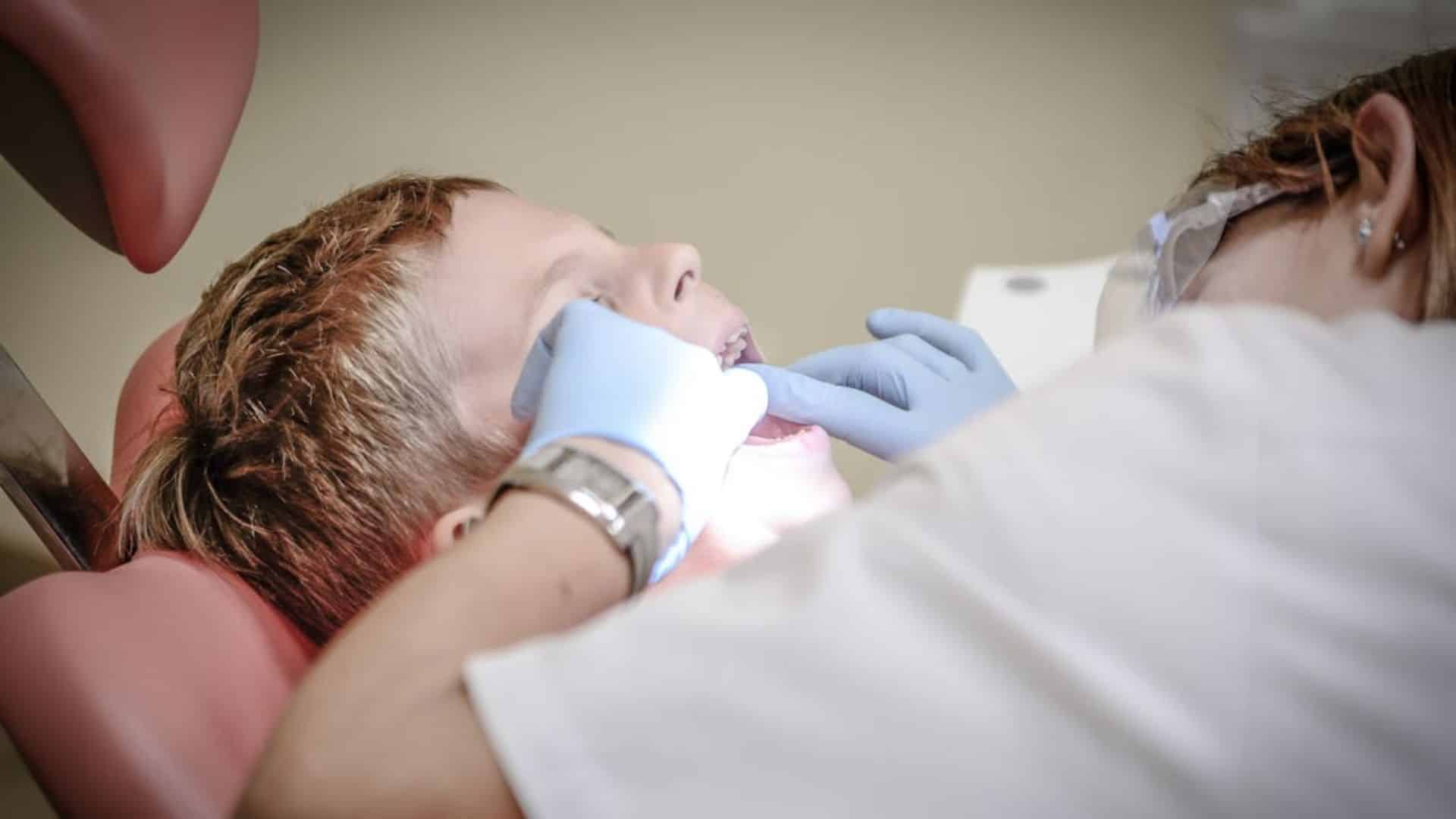 Dentist examining a young child's teeth in a dental chair.
