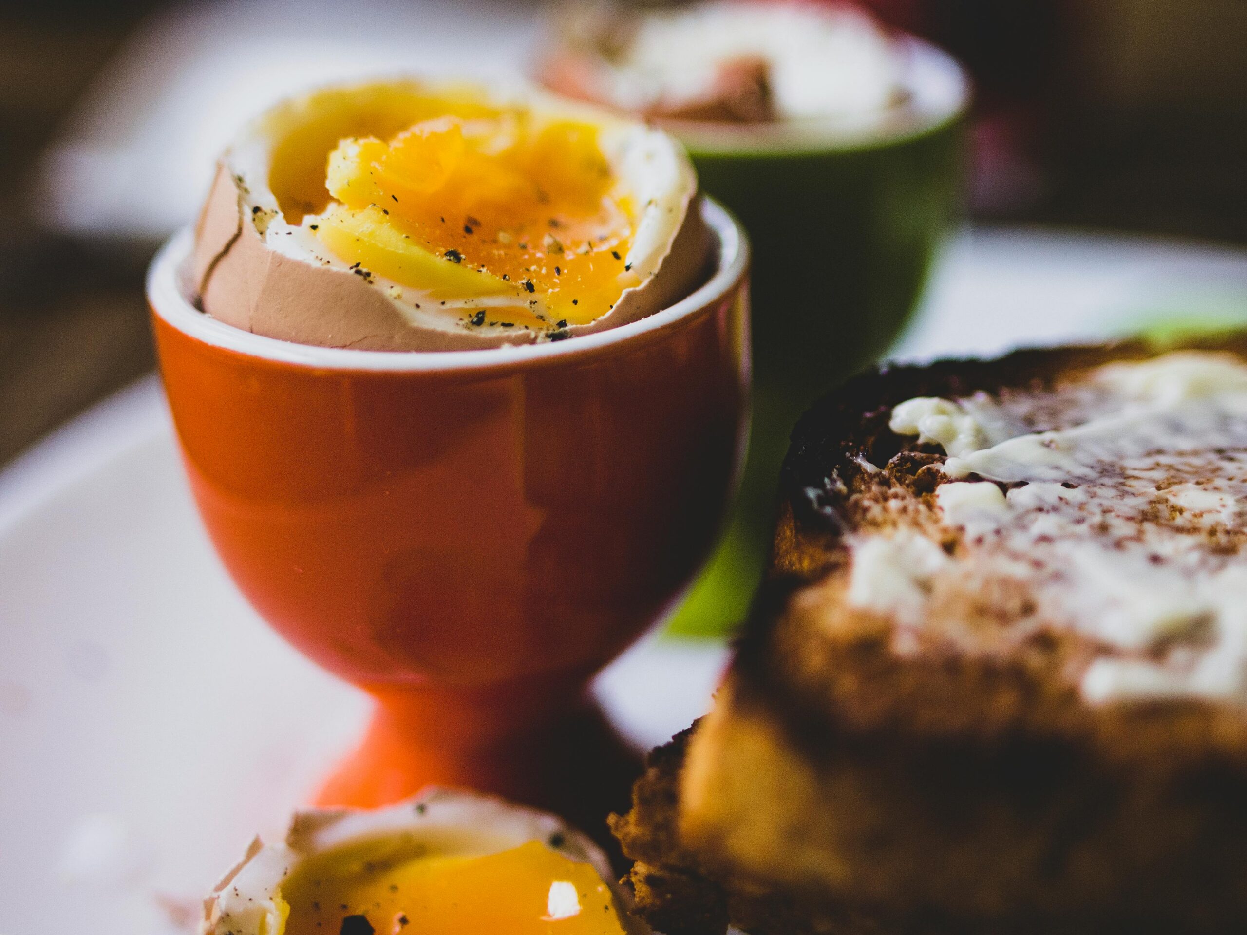 Soft-boiled egg in cup with runny yolk served alongside toast.