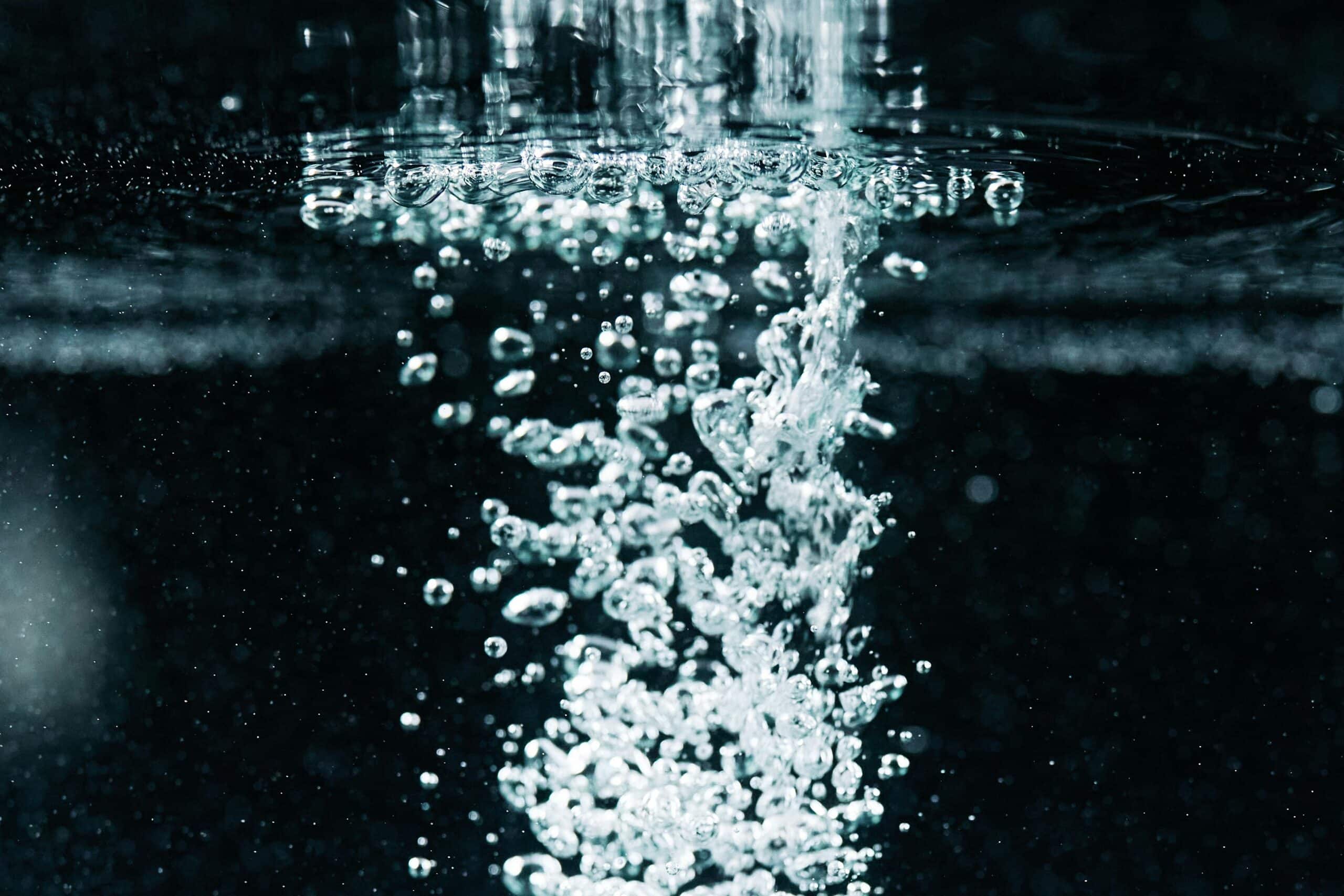 Air bubbles rising through water in a close-up underwater view.