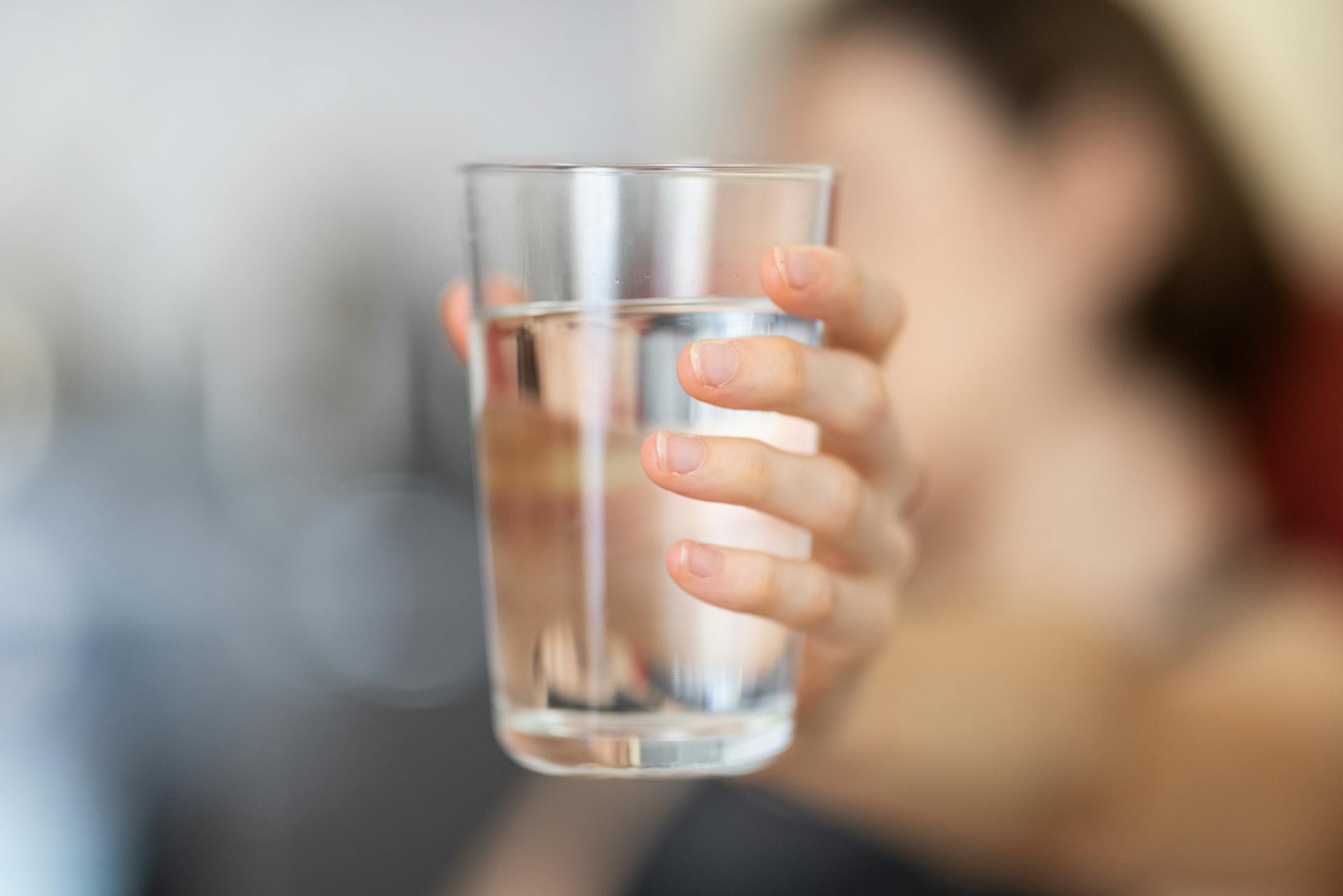 Hand of a young girl holding a clear glass of water up close with hand in focus.