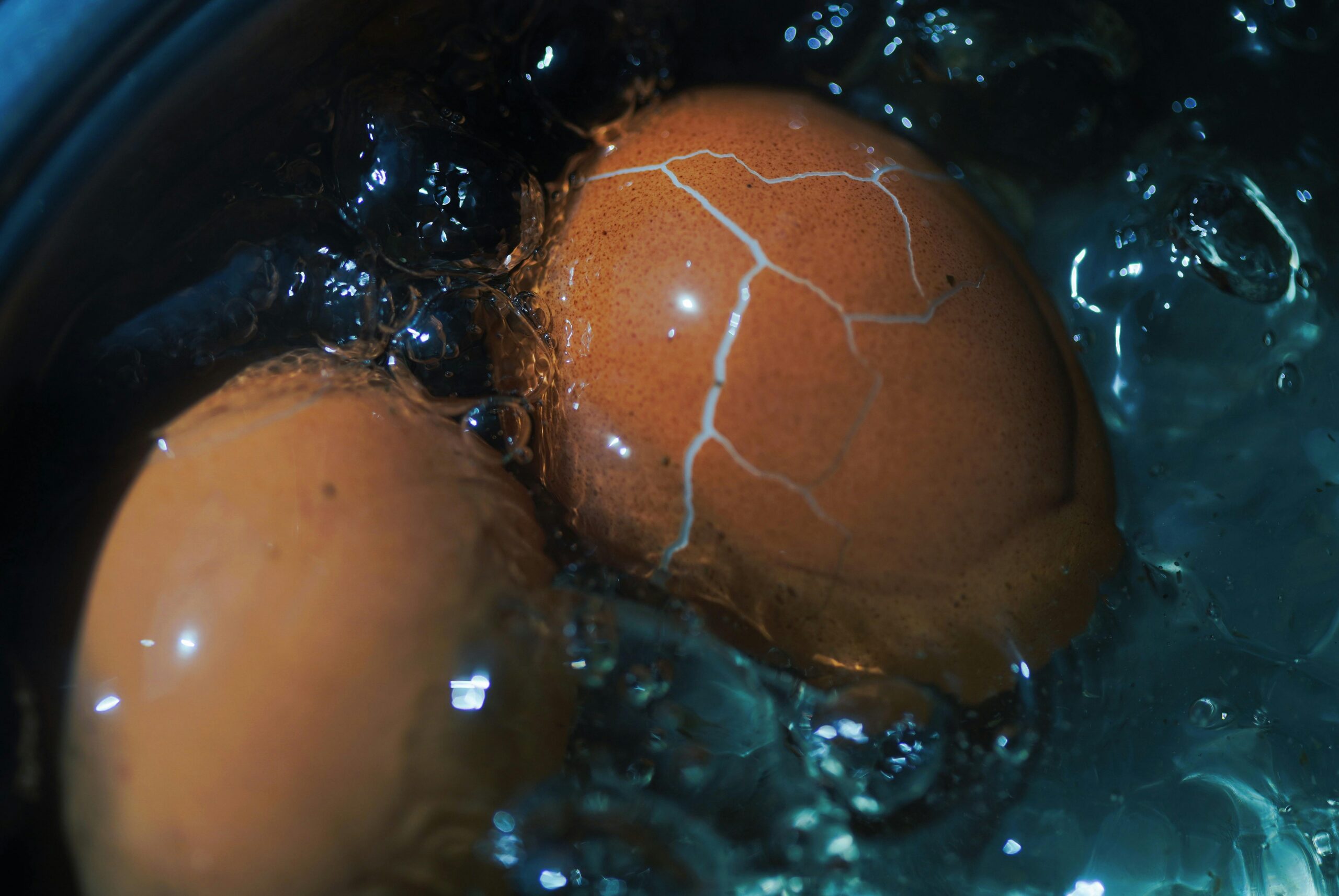 Cracked eggs boiling in water with bubbles forming around shells.
