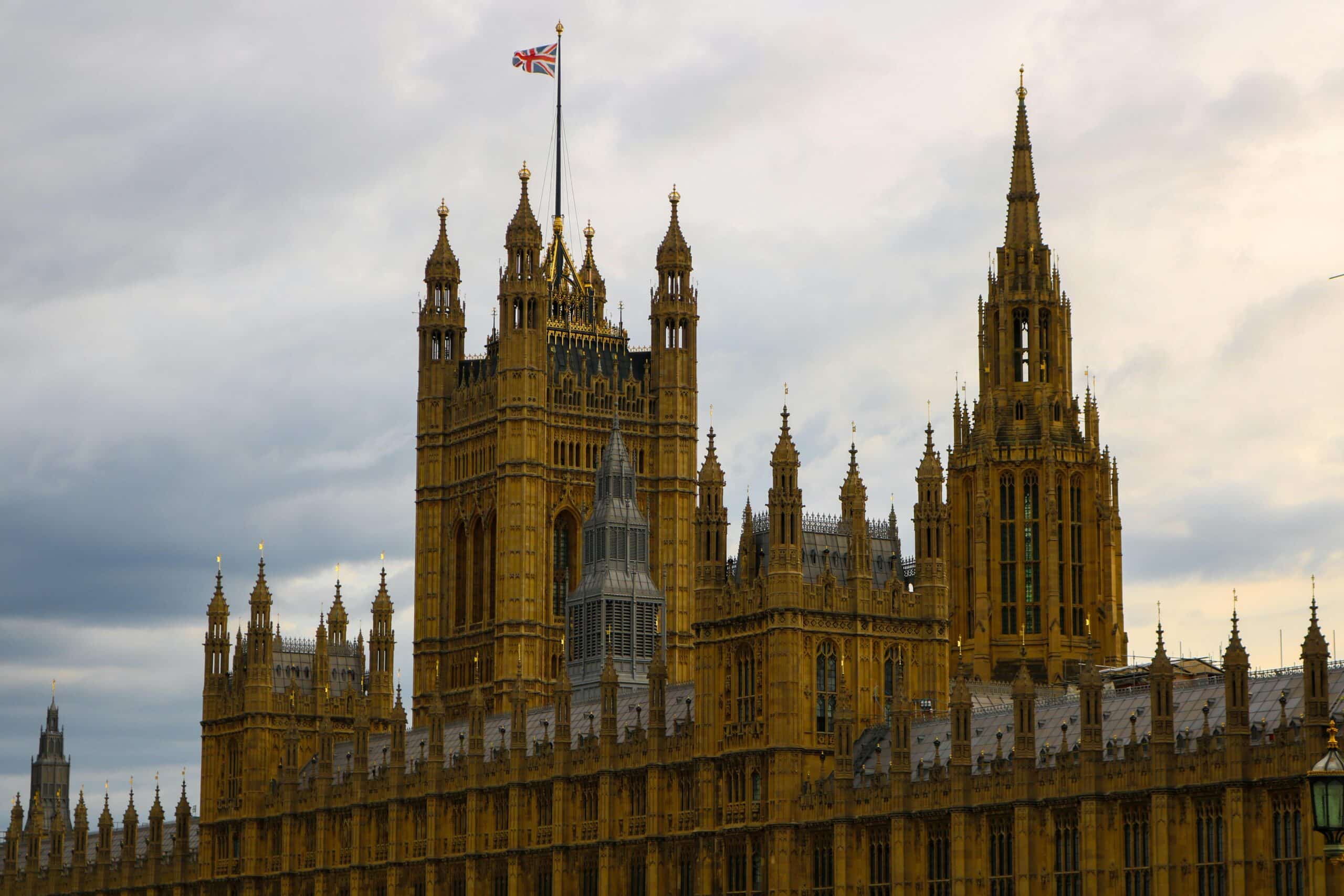 Houses of Parliament in London with Union Jack flag flying atop Victoria Tower under cloudy sky.