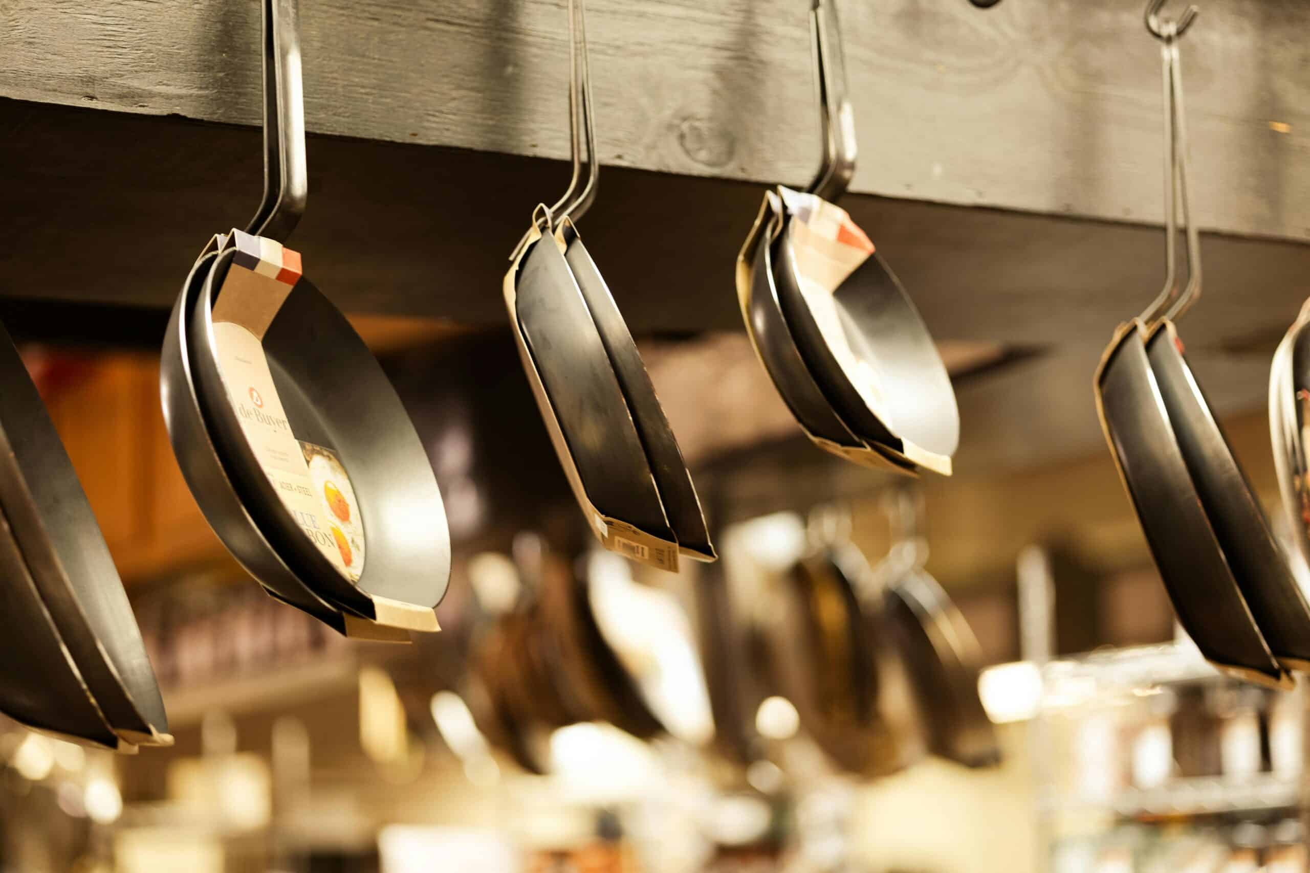 Nonstick frying pans hanging on hooks in a kitchen cookware display.