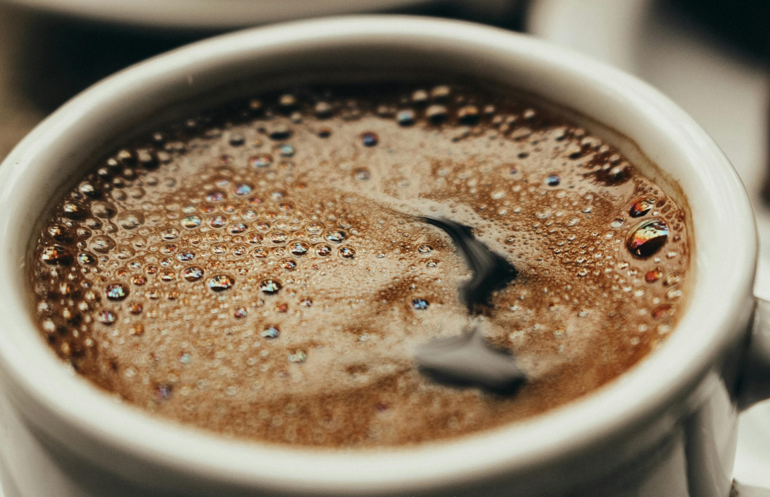 Close-up of black coffee with bubbles forming on the surface inside a white mug.