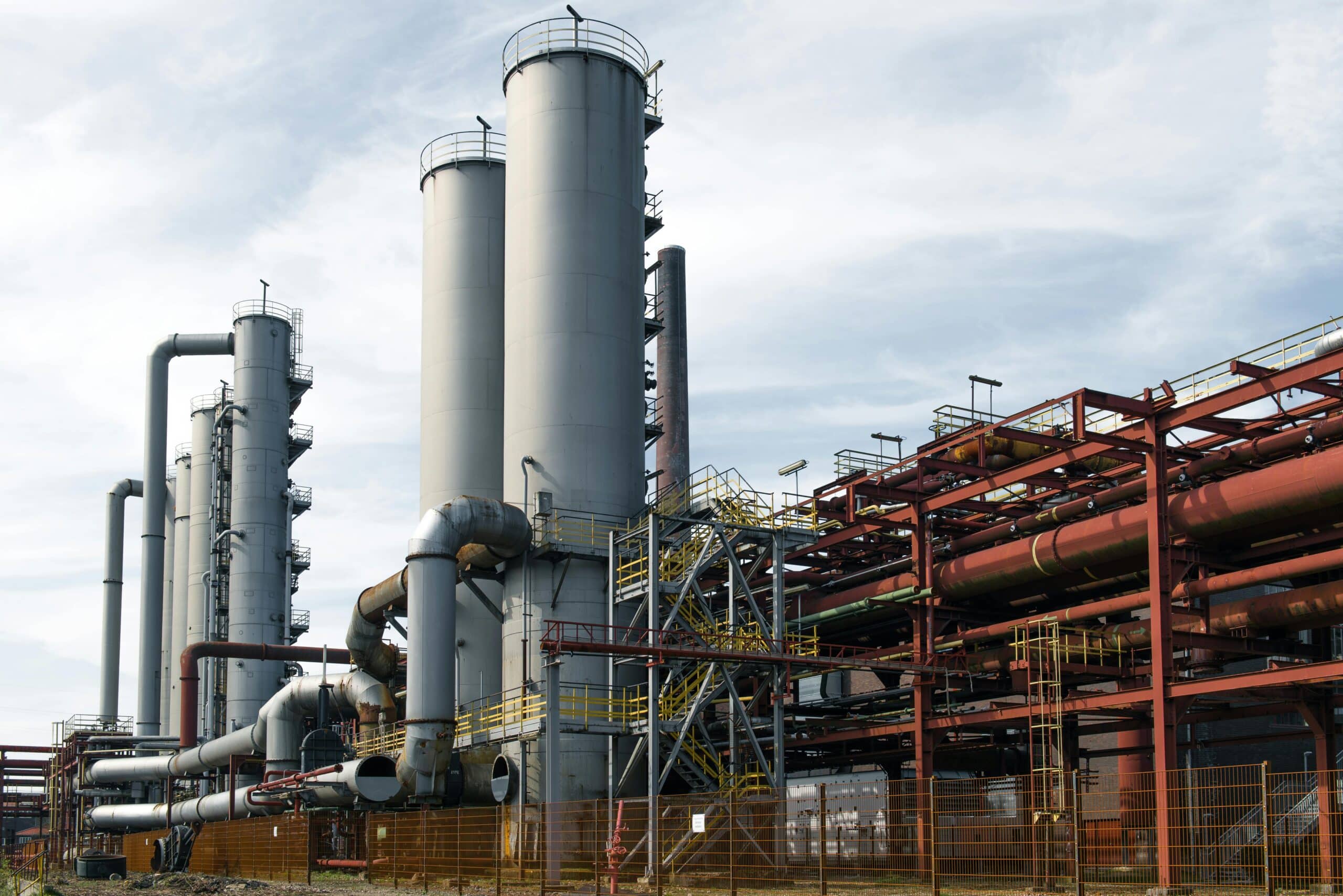 Industrial refinery with large storage tanks, pipes, and processing towers under a cloudy sky.