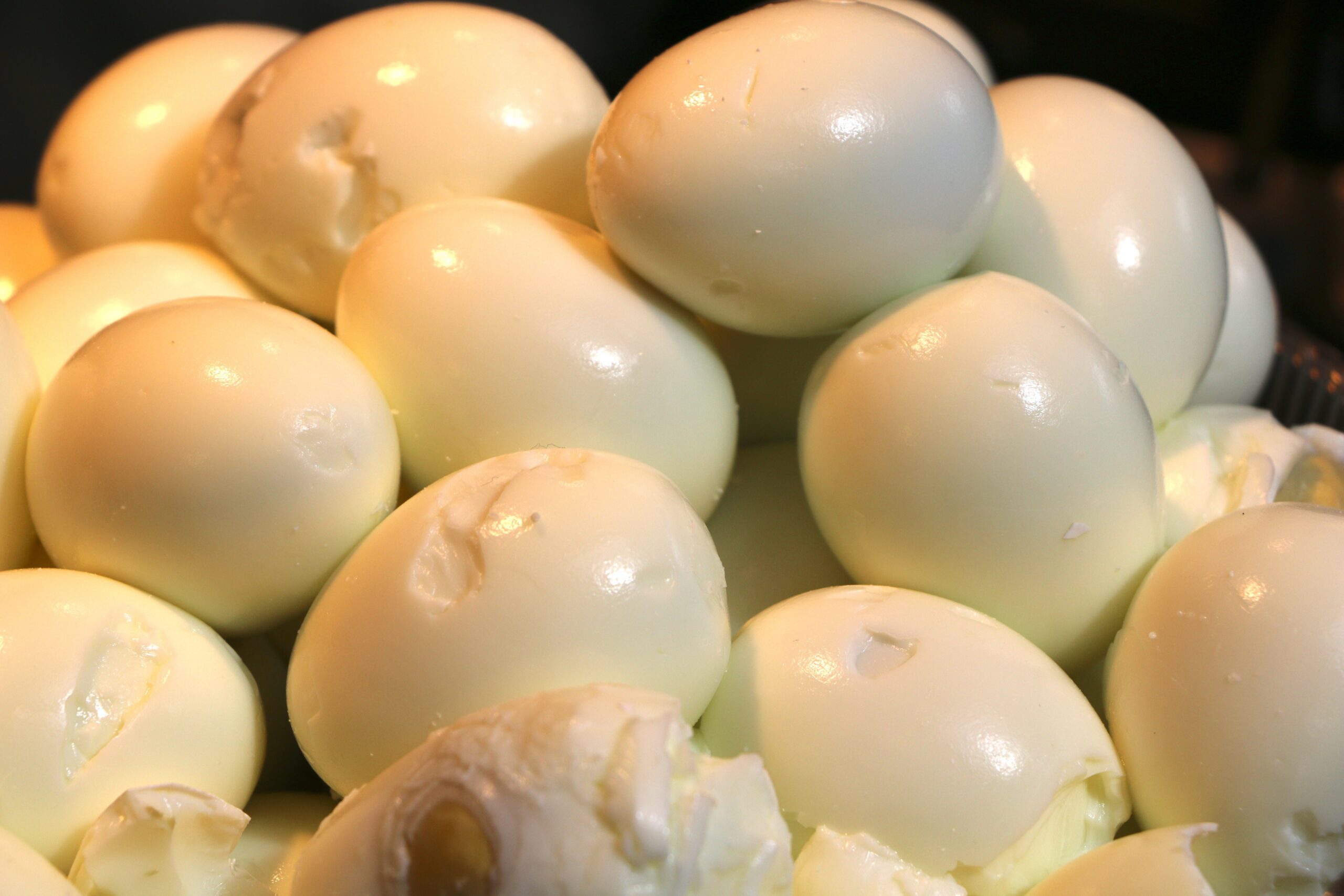 Pile of peeled hard-boiled eggs with dents on surfaces.