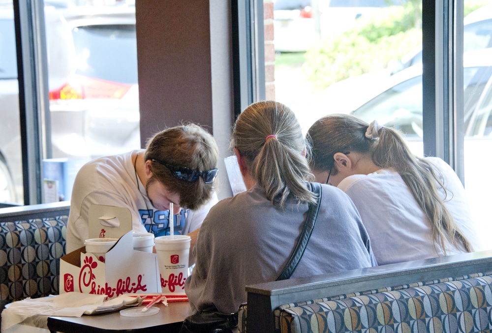 Three people seated at a Chick-fil-A booth looking down at table with food and drinks.