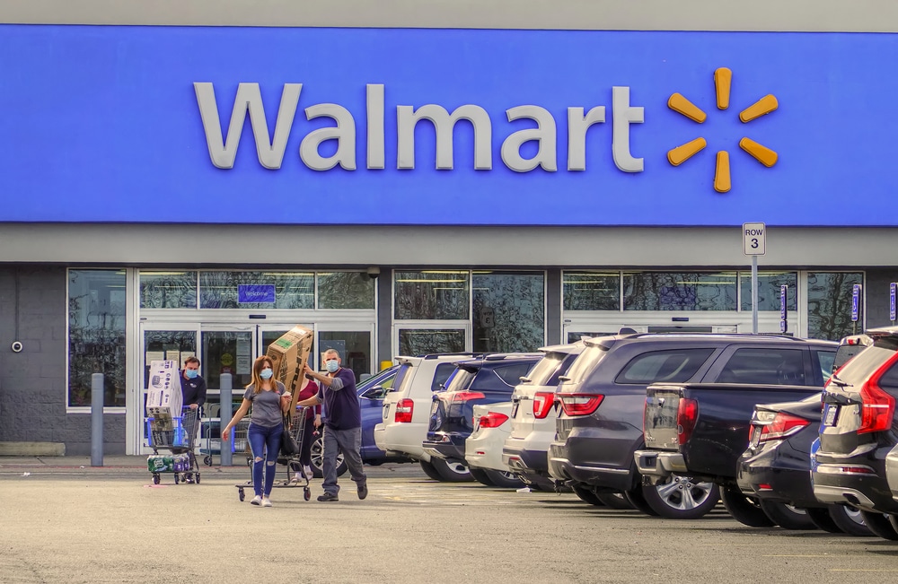Shoppers exit Walmart store pushing carts in parking lot.