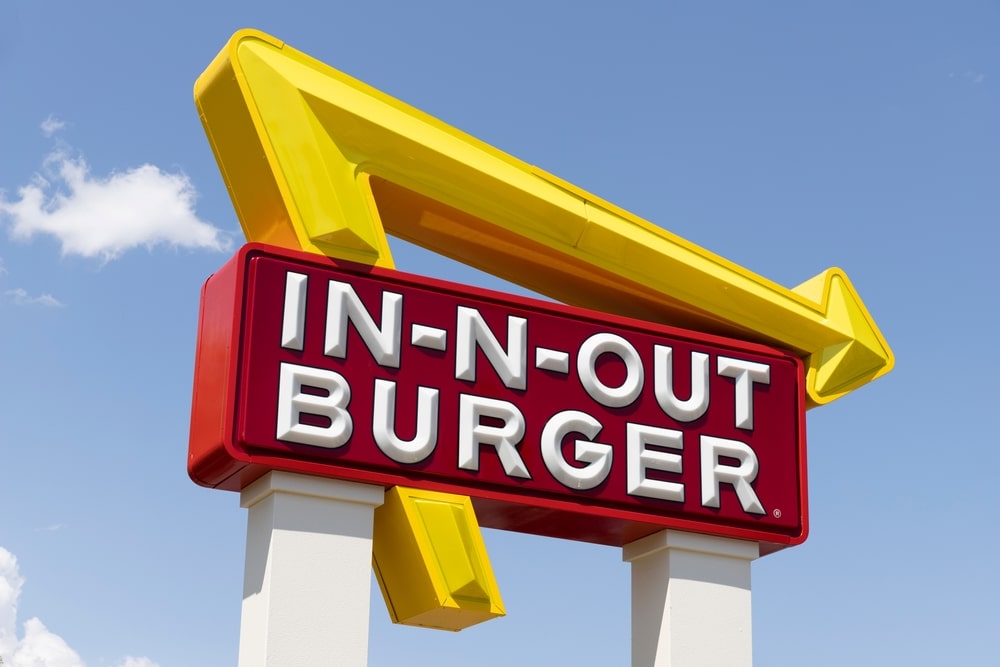 In-N-Out Burger sign with signature yellow arrow against a blue sky.