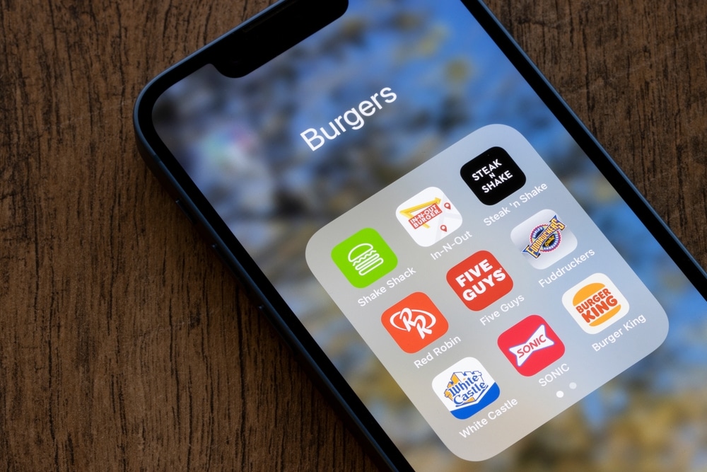 Smartphone displaying a folder of burger restaurant apps including Shake Shack, In-N-Out, and Five Guys.
