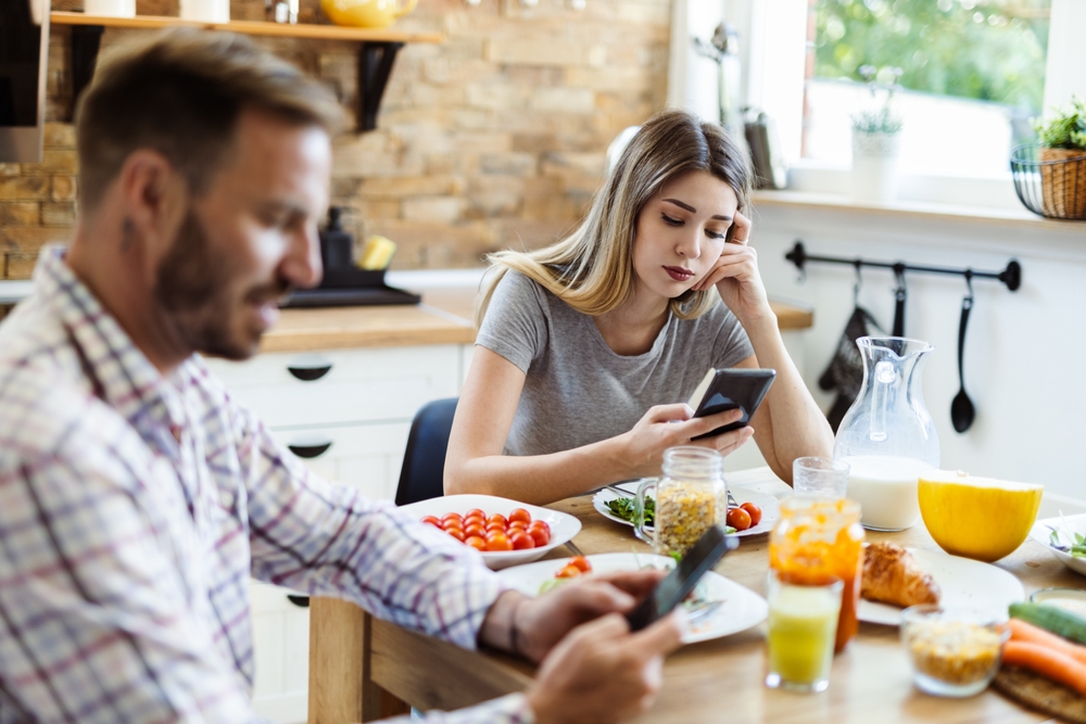 Man and woman sitting at the dining table using smartphones during a meal.