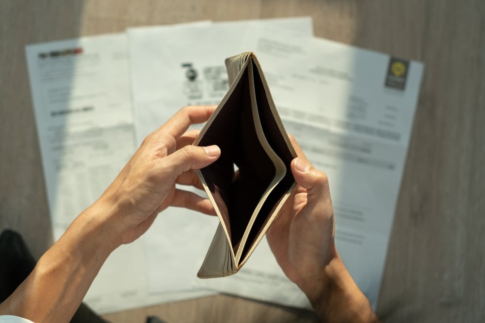 A person's hands opening an empty wallet above household bills spread on a table.