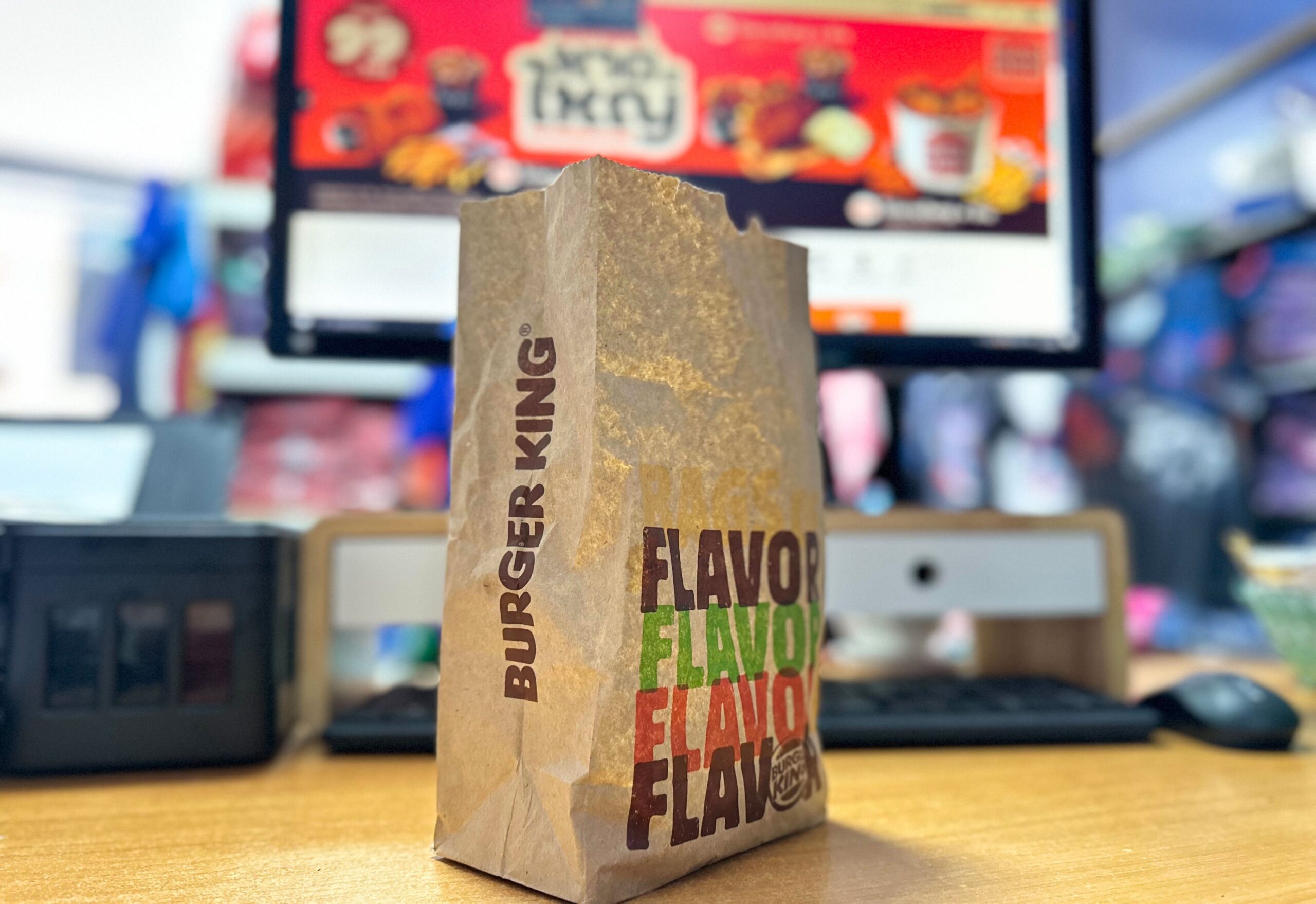 Burger King takeout bag on desk in front of computer screen.