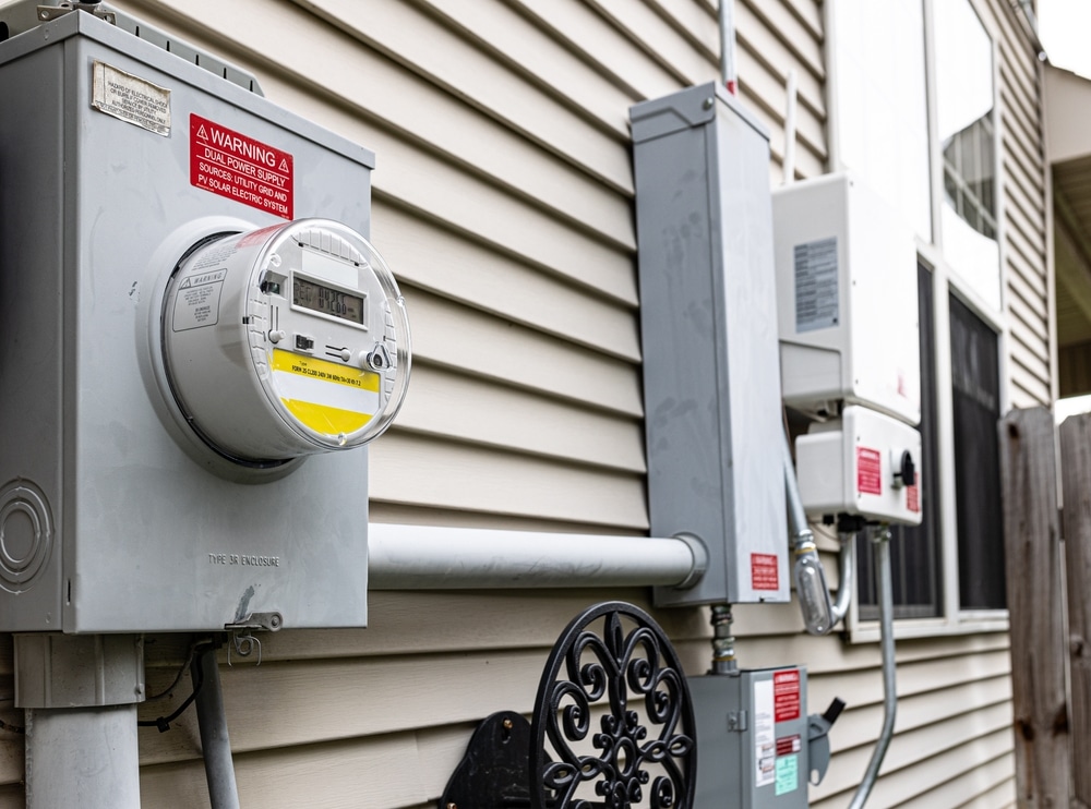 Electric utility meter mounted on exterior house wall.
