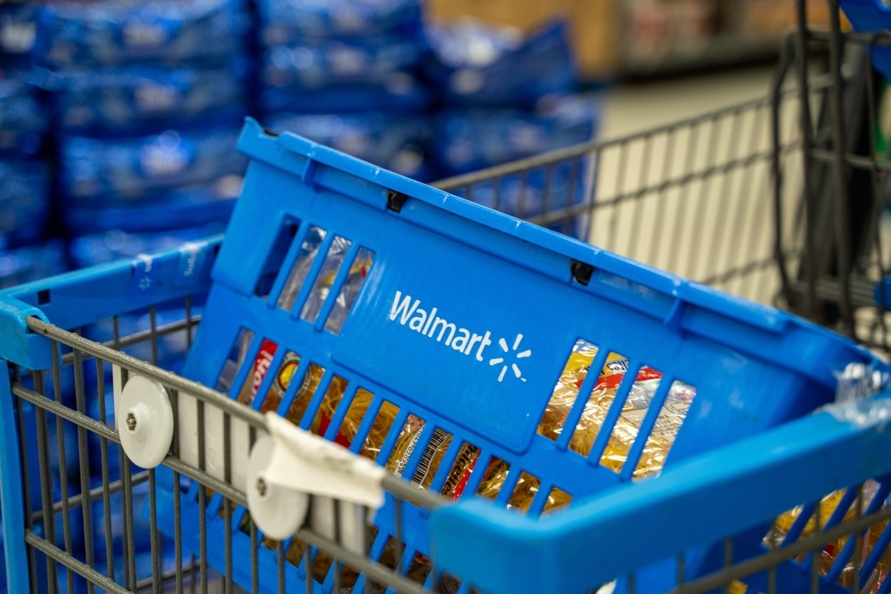 Walmart shopping cart with blue basket filled with packaged groceries in store aisle.