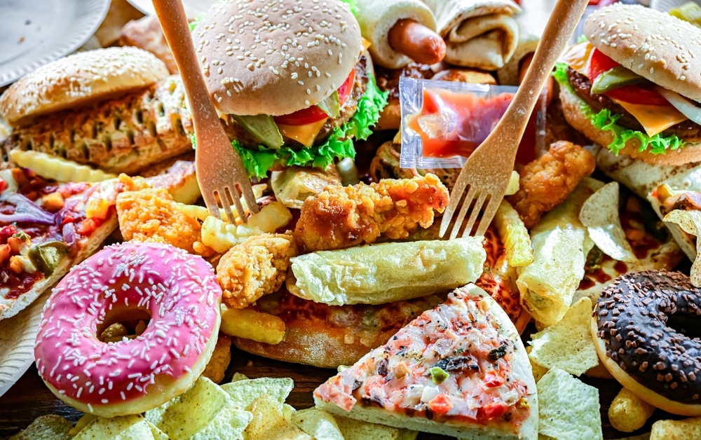 Assortment of fast food including burgers, fried chicken, pizza, fries, and doughnuts on table.