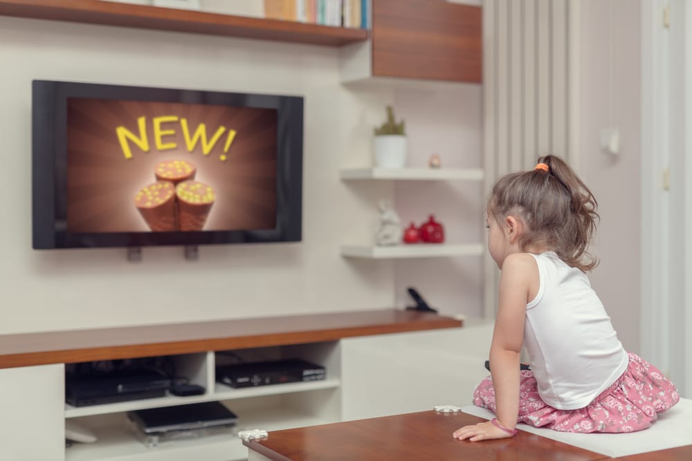 Child sitting on table watching TV displaying new ice cream advertisement.