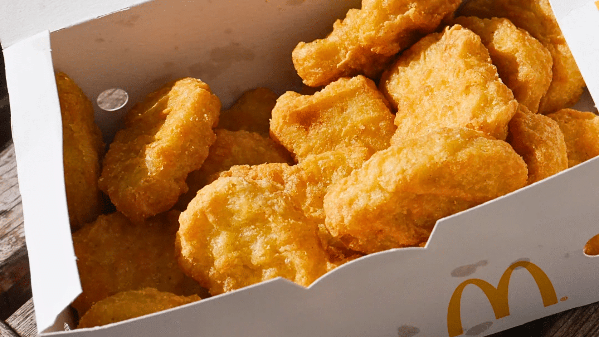 A close-up, top-down shot of a crisp white cardboard box completely filled with golden-brown, crispy Chicken McNuggets.