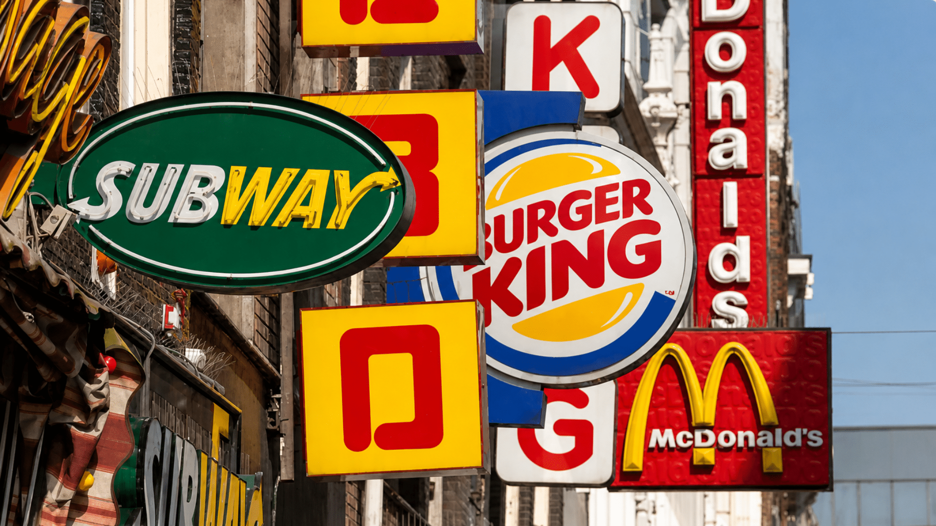 Subway, Burger King, and McDonald’s signs displayed along a busy city street.