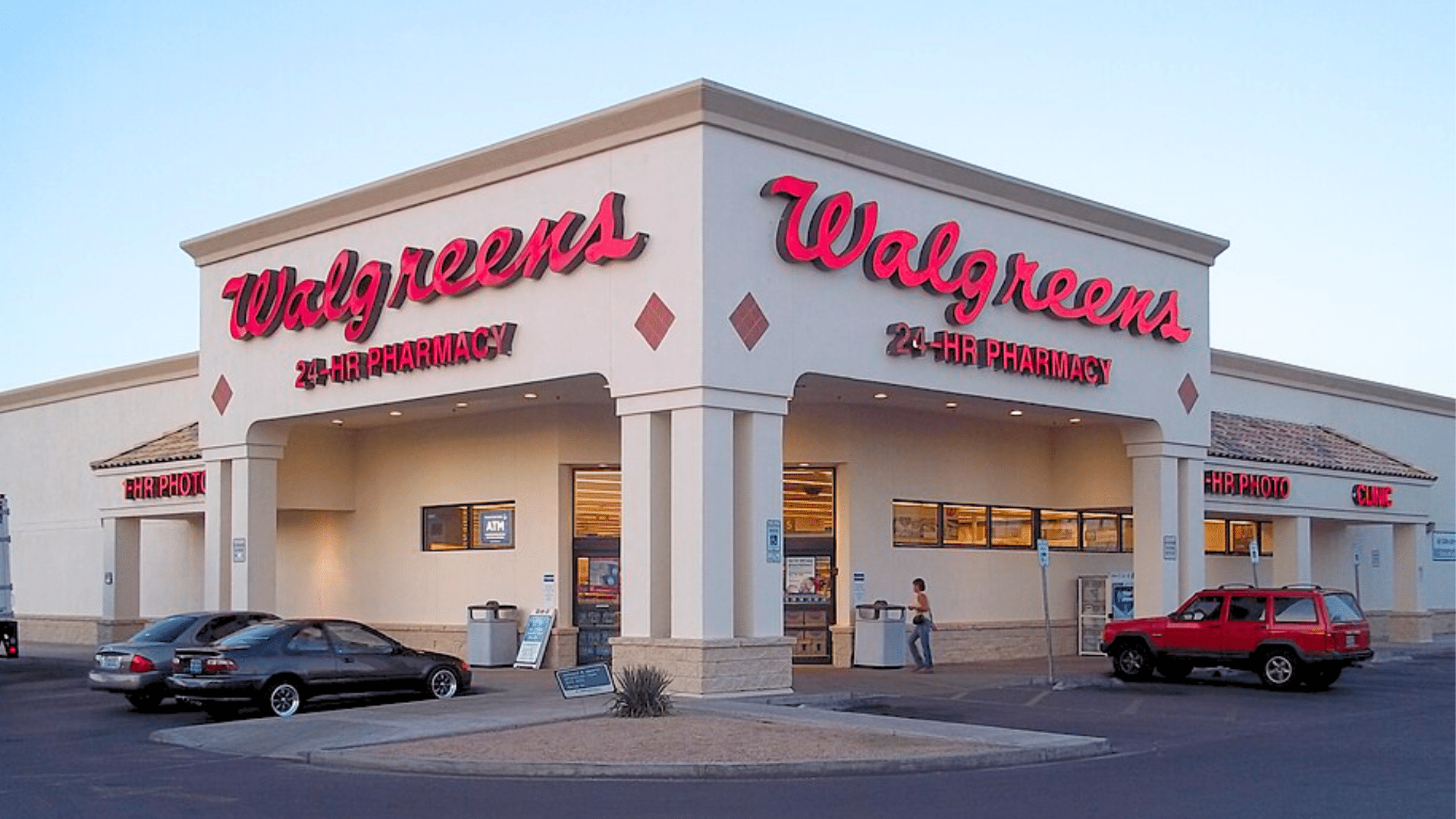 The exterior of a white Walgreens store building with bright red neon signs reading "Walgreens 24-HR PHARMACY."