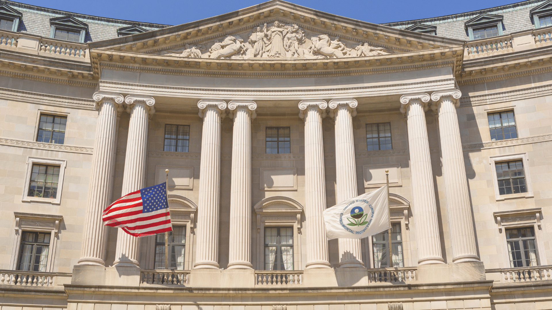 The classic columned exterior of the Environmental Protection Agency building flying the United States and EPA flags.