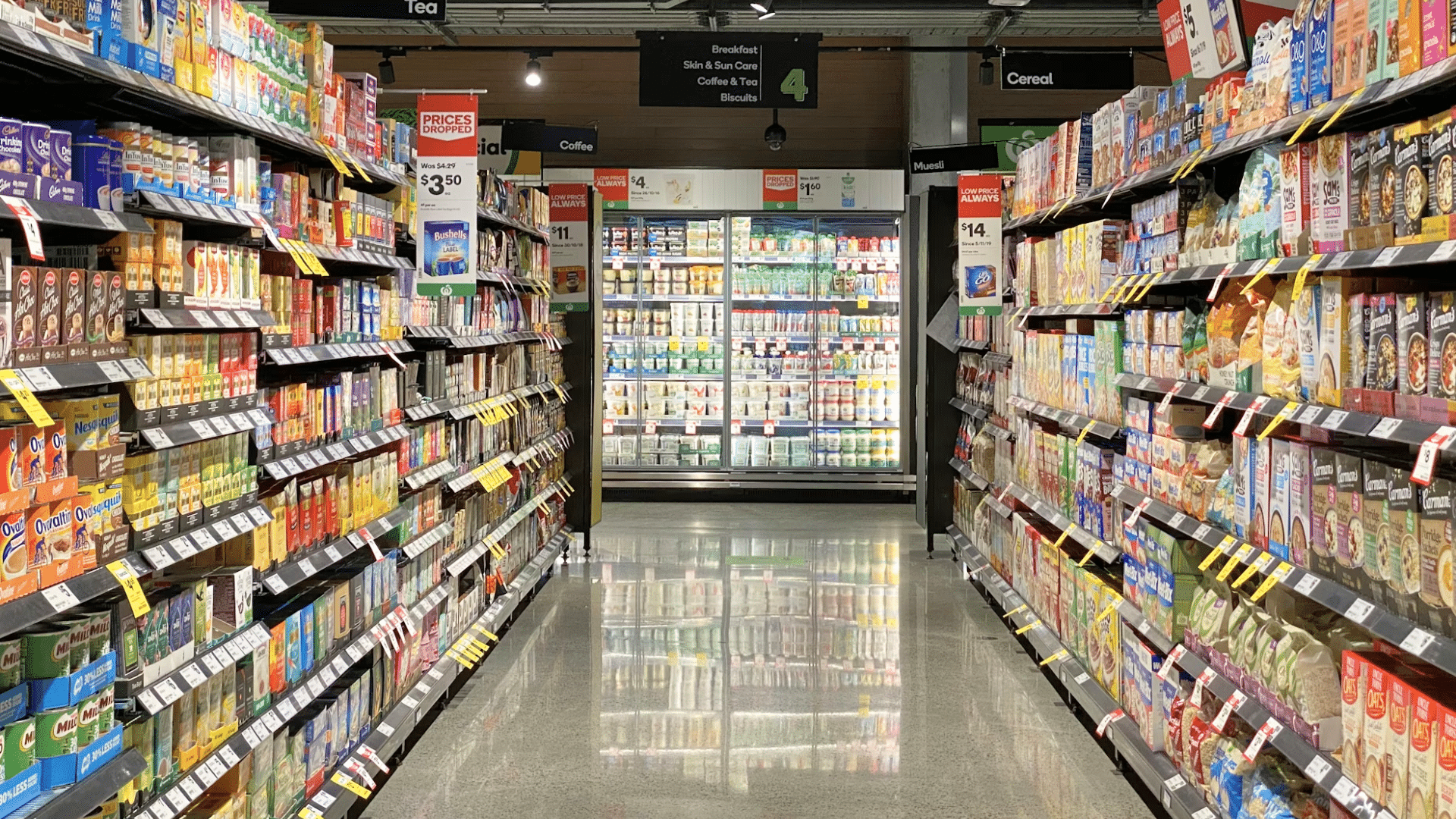 A long, brightly lit grocery store aisle filled with fully stocked shelves and a shiny floor.
