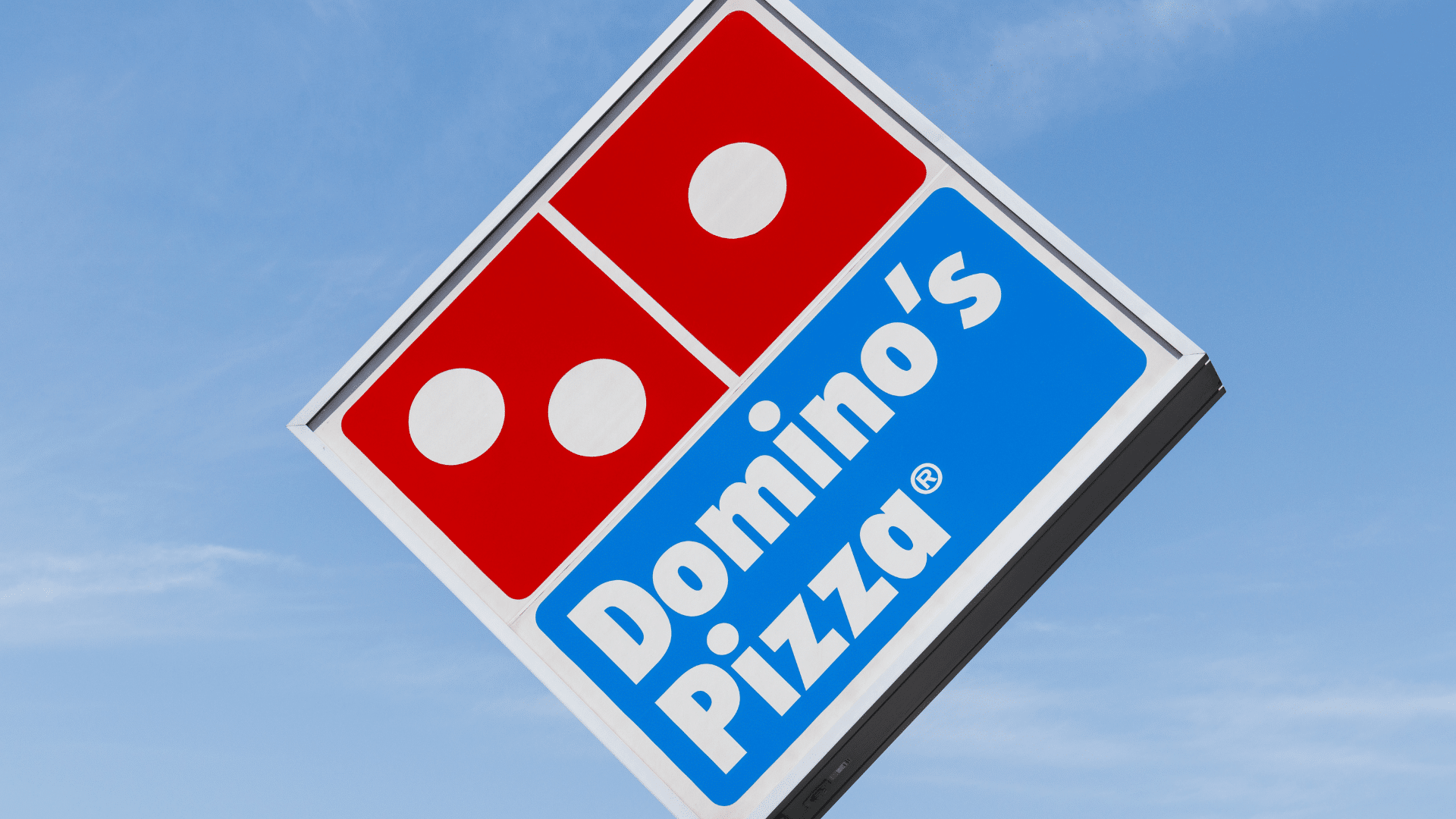 A tilted Domino's Pizza sign against a clear blue sky.
