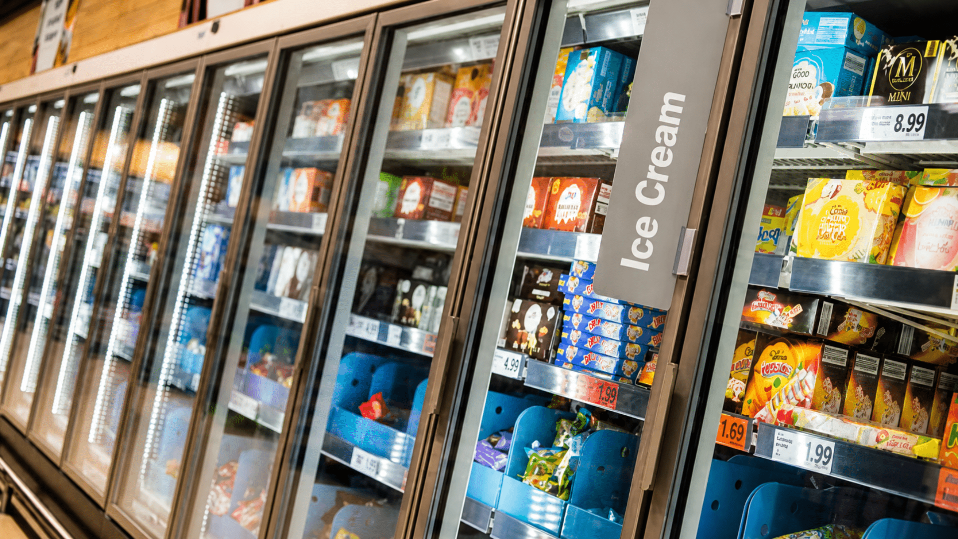 Supermarket freezer aisle stocked with packaged ice cream behind glass doors.