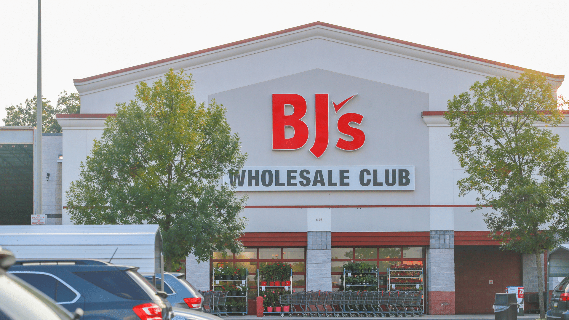The storefront of a BJ's Wholesale Club with its red logo above the glass entrance doors.
