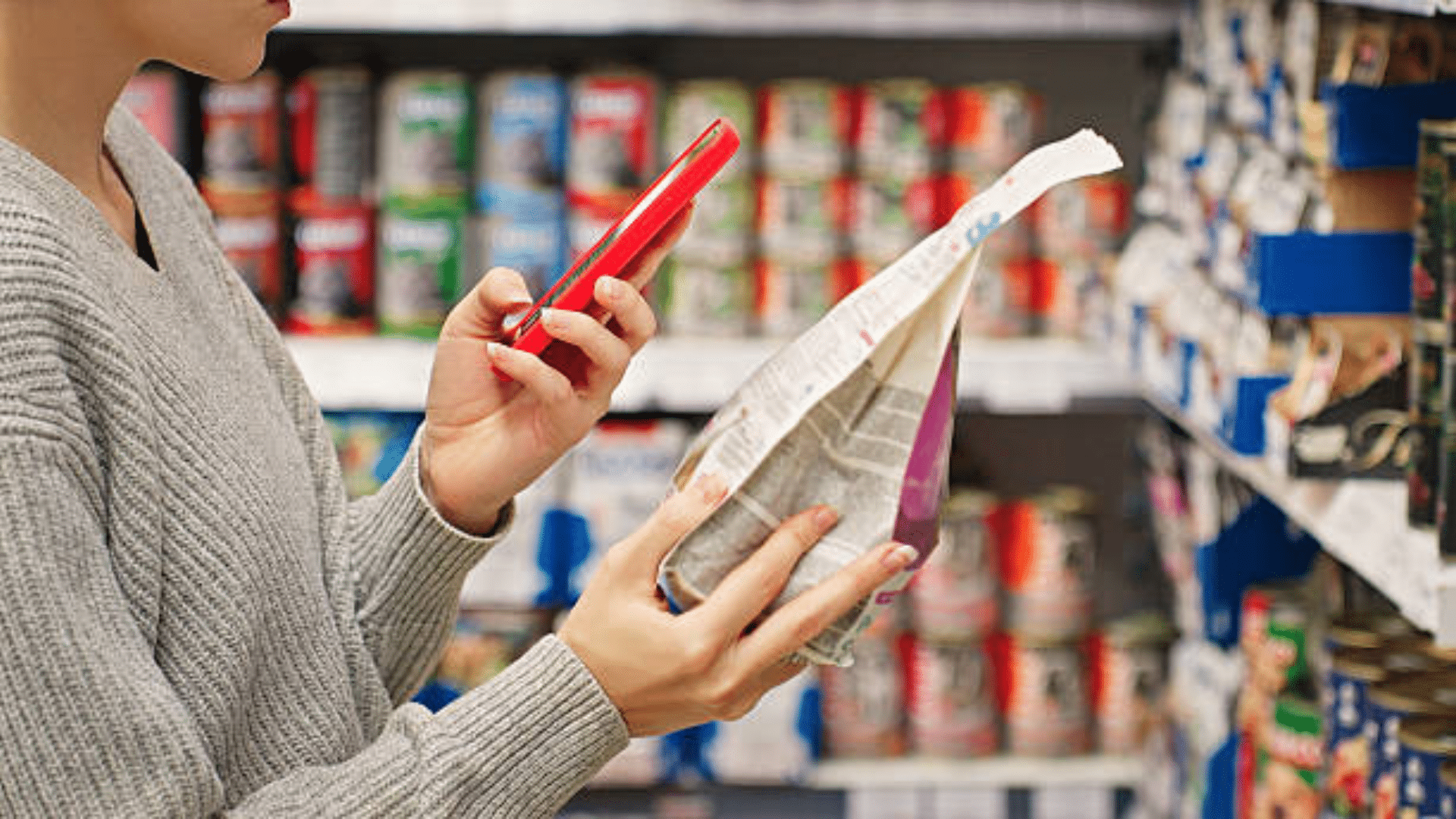Shopper checking a grocery item with a smartphone in a store aisle.
