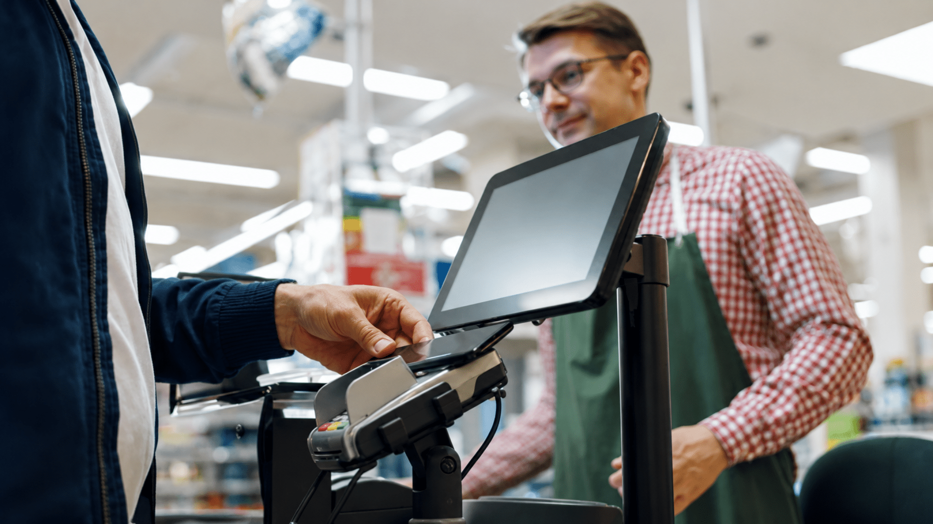 Customer tapping payment card at grocery store checkout terminal.