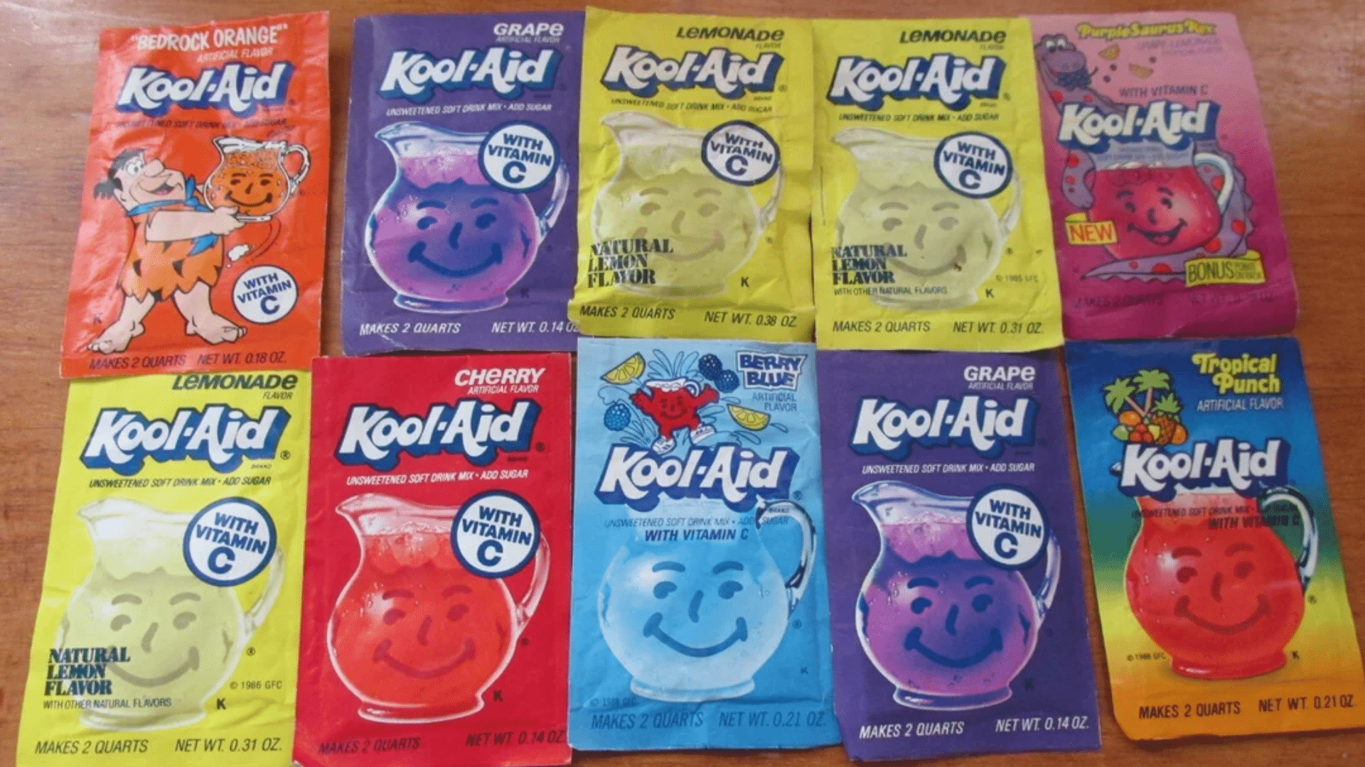 A top-down layout of ten vintage and modern Kool-Aid packets in various flavors like Bedrock Orange, Grape, Lemonade, Cherry, Berry Blue, and Tropical Punch, showcasing the brand's colorful history.