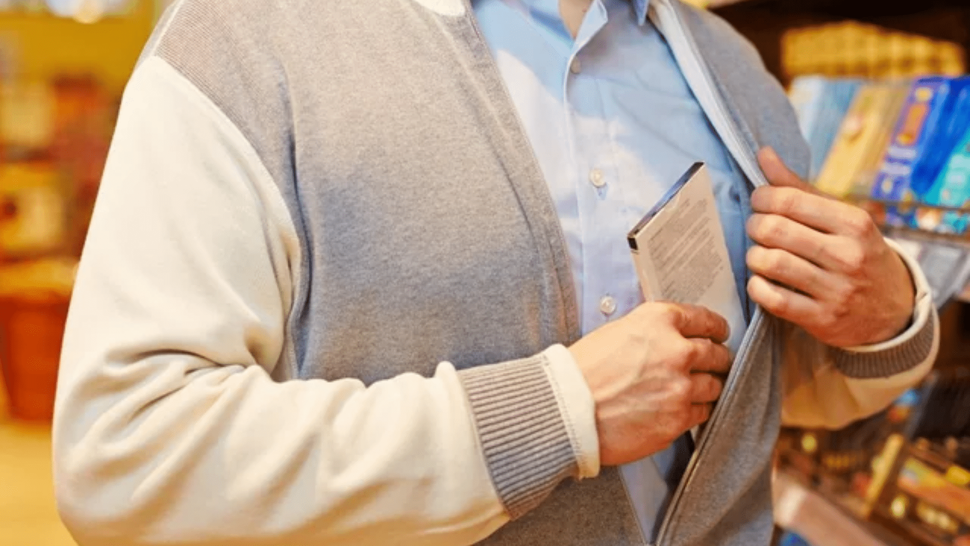Shopper concealing book inside jacket in bookstore aisle.