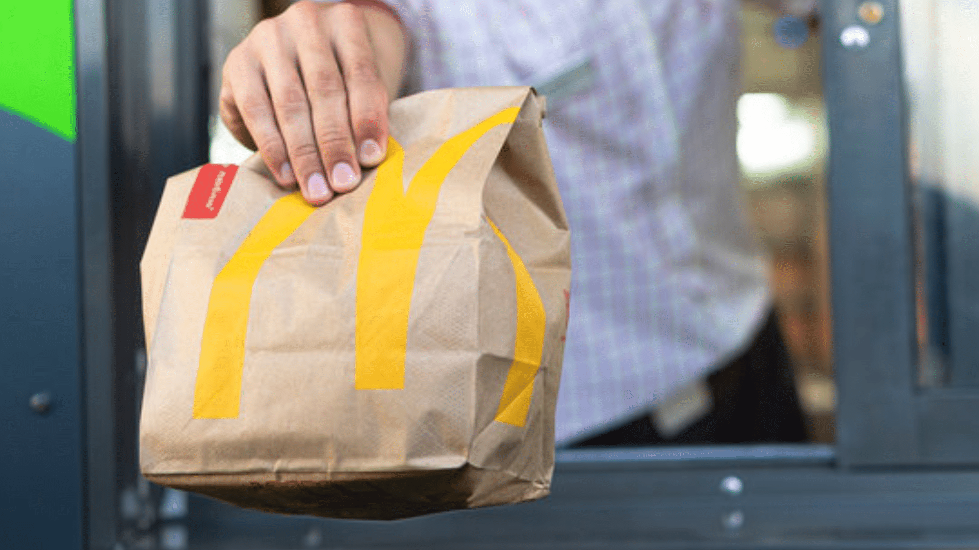 Customer receiving a McDonald’s takeout bag through a drive-thru window.
