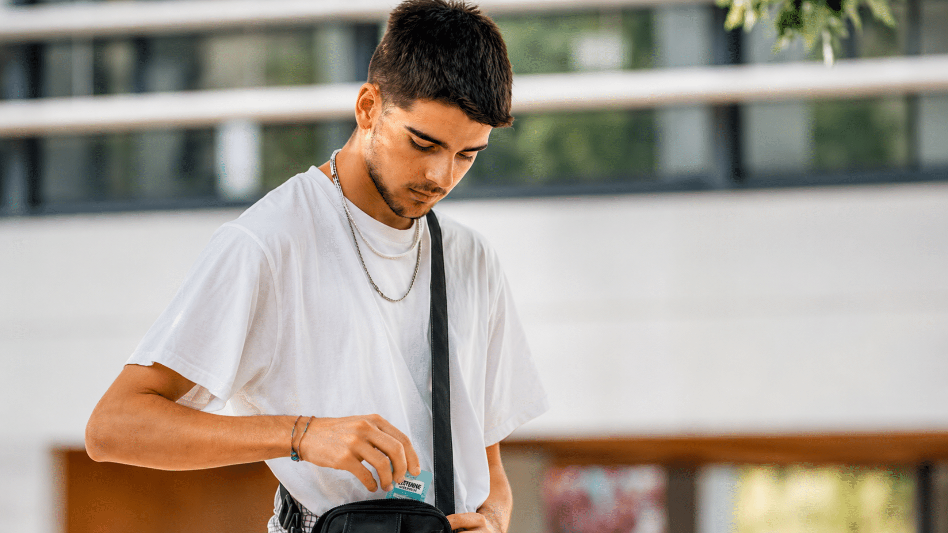 Young man placing a nicotine pouch packet into a black crossbody bag.