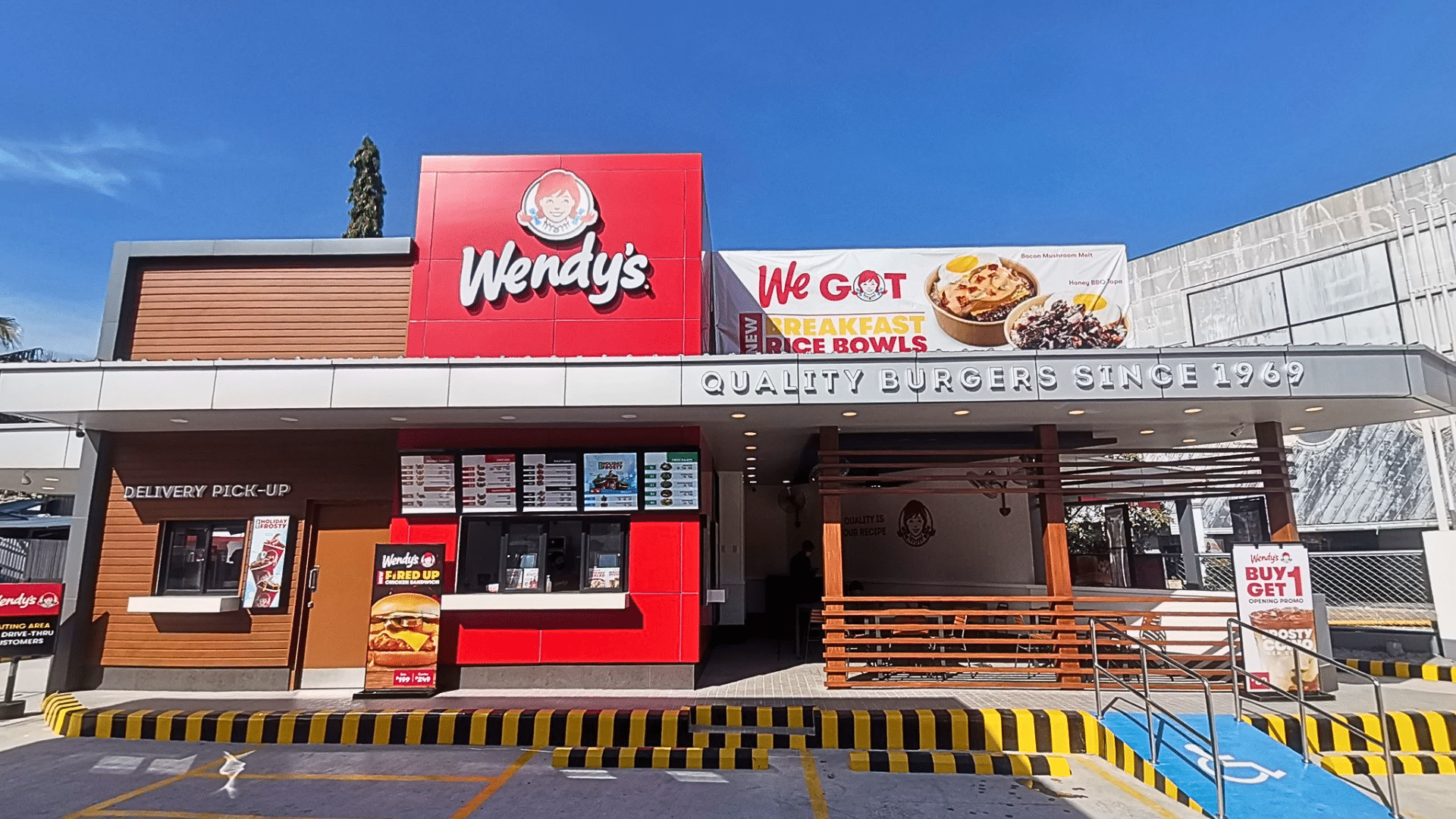 A daytime street-level shot of a modern Wendy’s restaurant featuring a red-and-brown wood exterior.