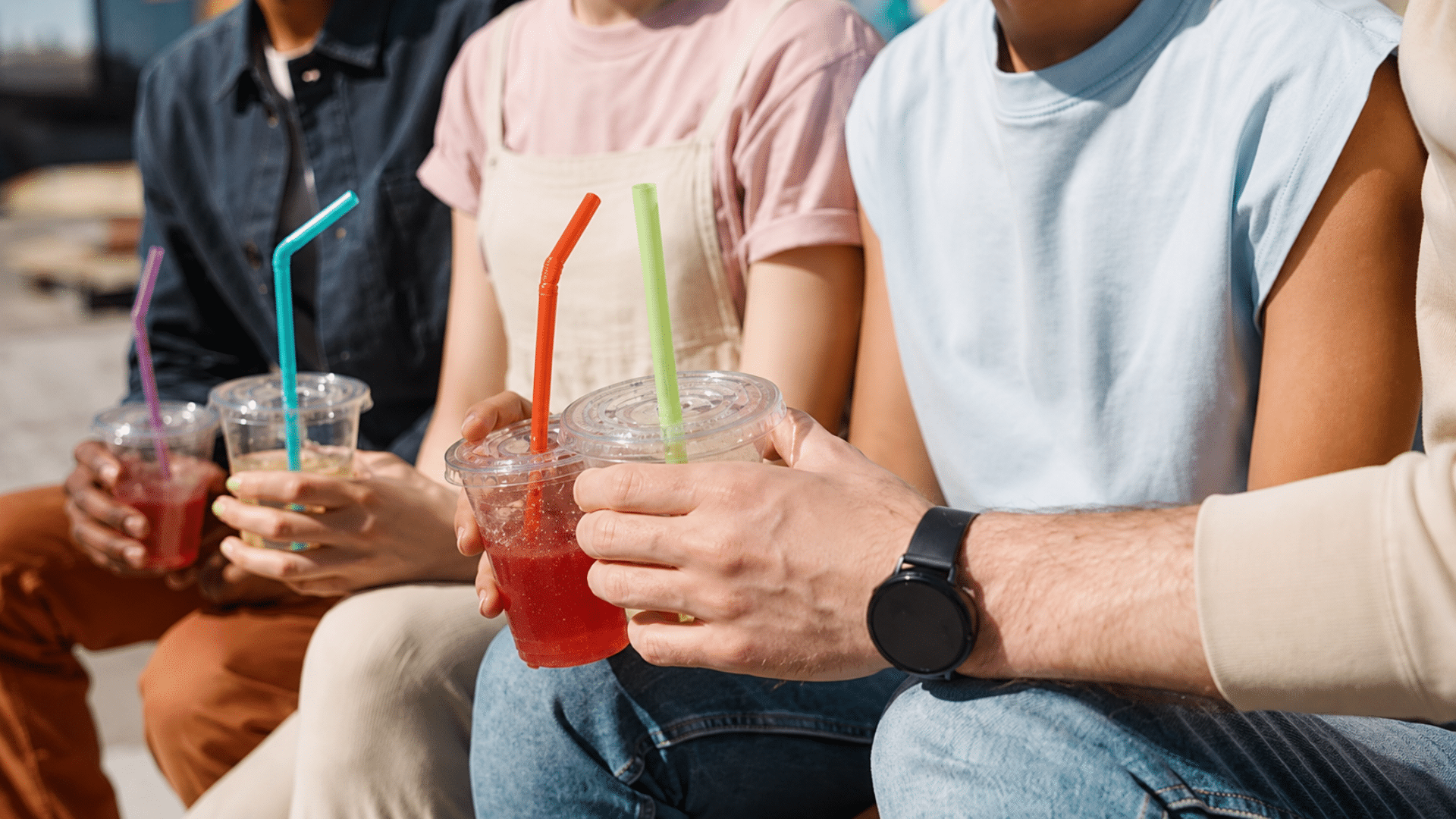 Group of people holding colorful drinks in plastic cups outdoors.