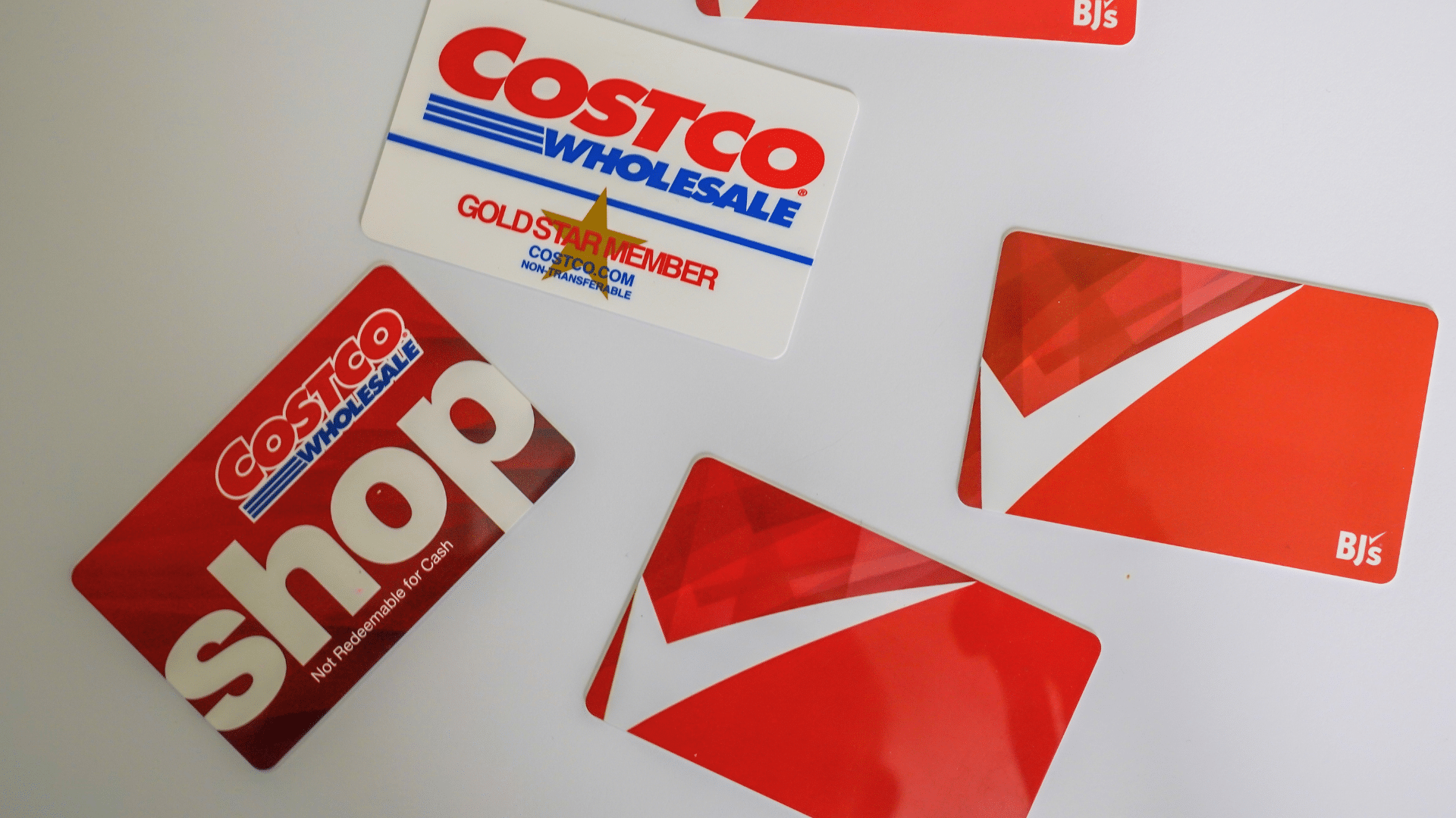 An assortment of Costco and BJ's Wholesale Club membership and shopping cards scattered on a white surface.