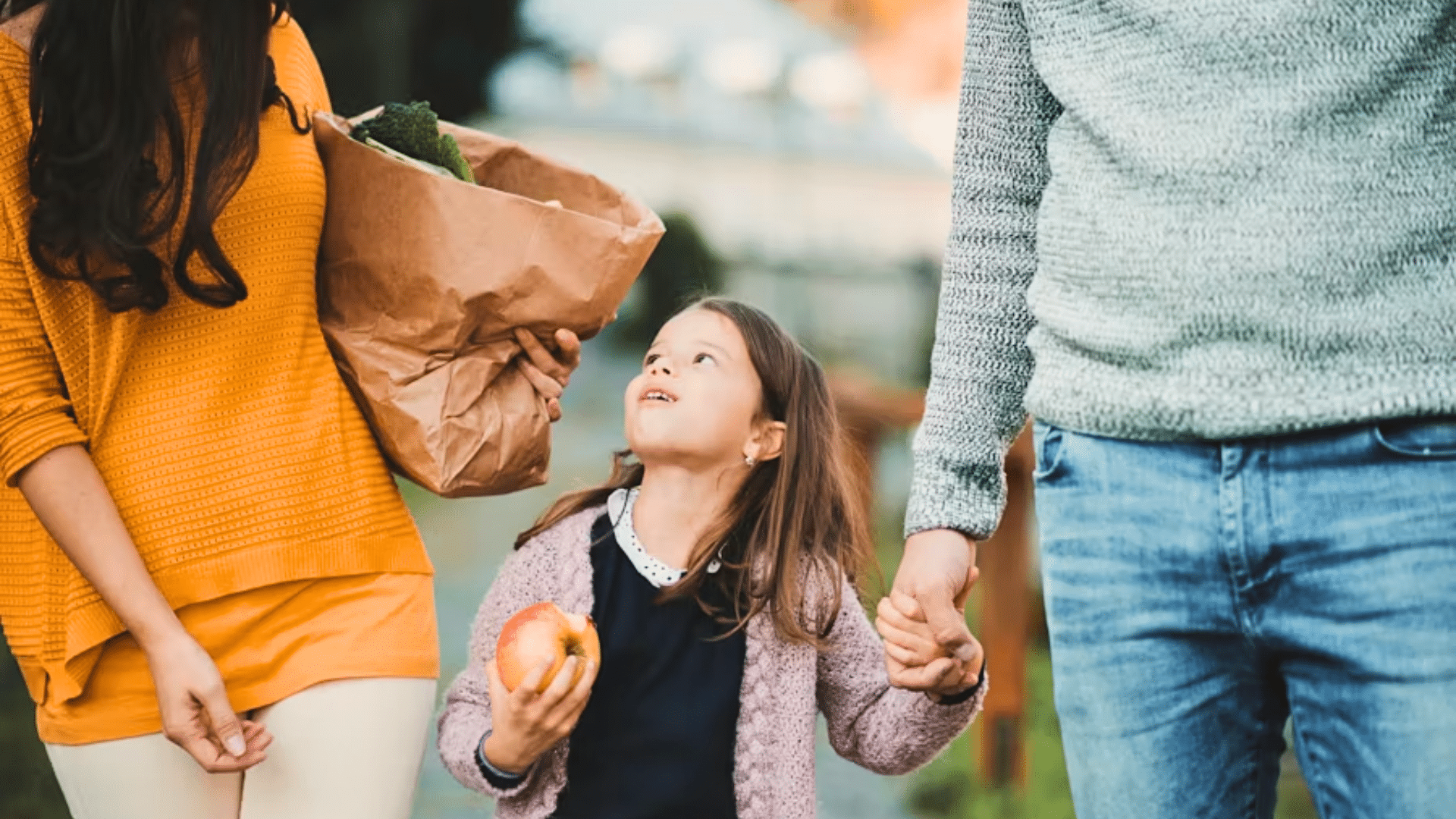 Family walking with groceries while child holds an apple outdoors.