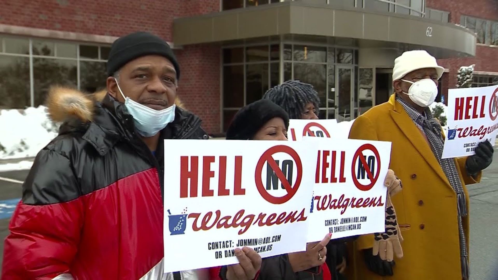 Group of protesters standing outside a commercial building in winter clothing and face masks while holding signs that read “HELL NO Walgreens.”