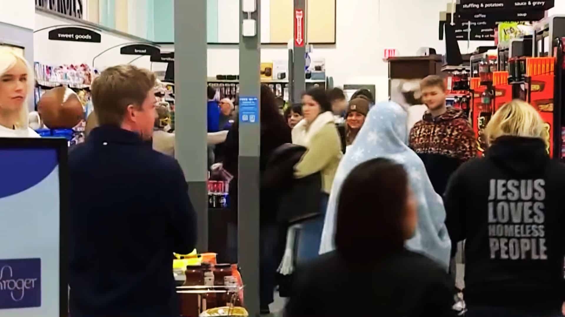 Busy Kroger grocery store interior filled with shoppers walking through aisles and checkout areas during a crowded shopping period.