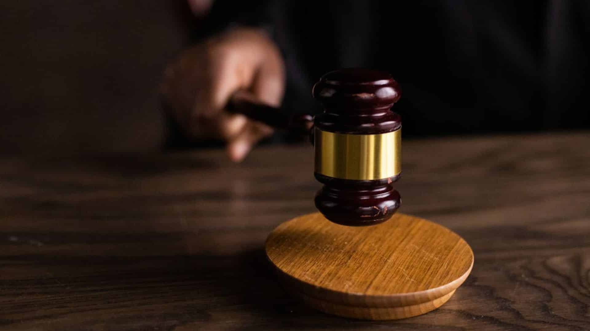 A judge's gavel about to strike a wooden sound block on a dark wood table.