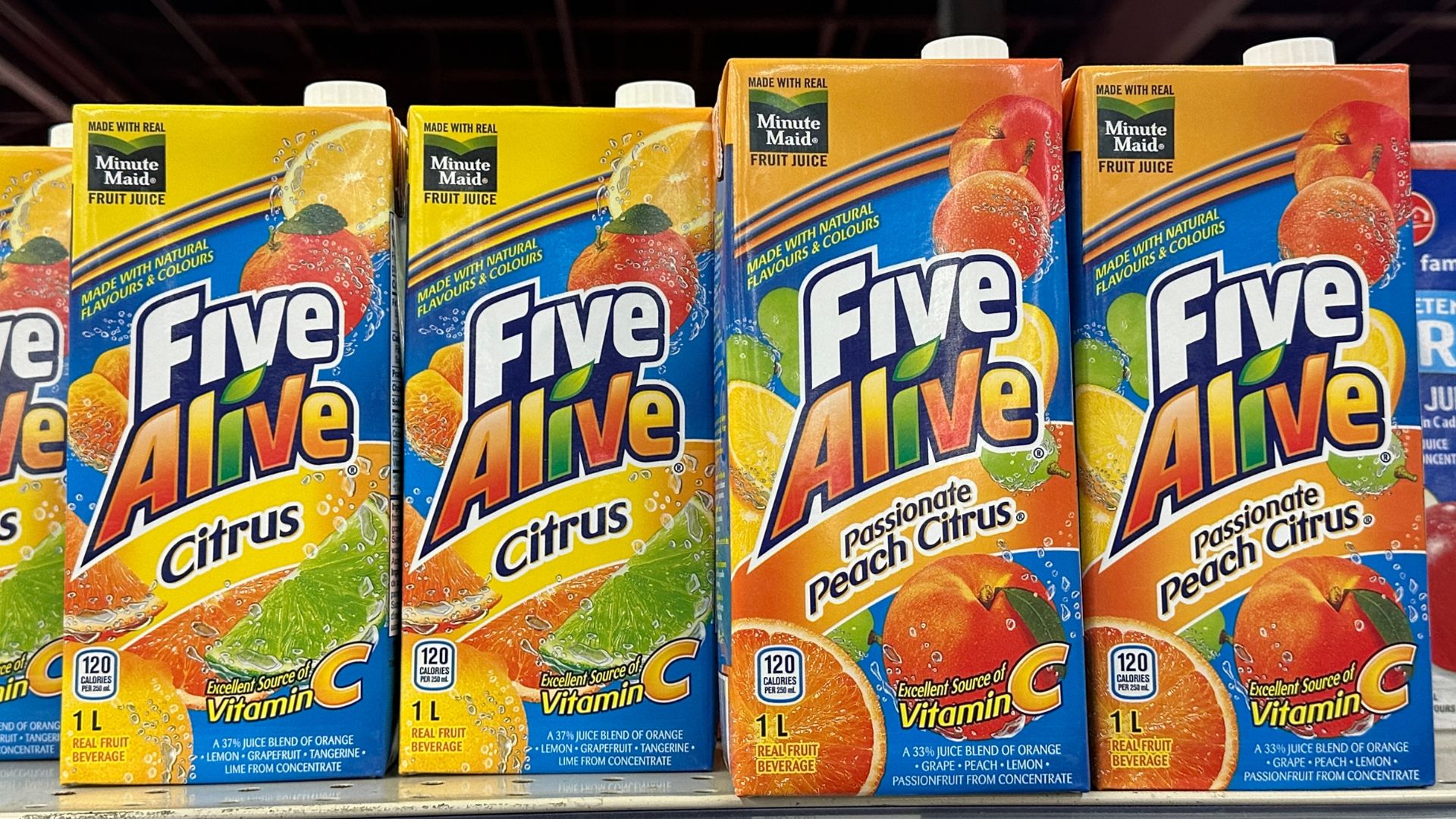 Cartons of Five Alive Citrus and Passionate Peach Citrus fruit juice lined up on a grocery store shelf with colorful citrus fruit graphics on the packaging.