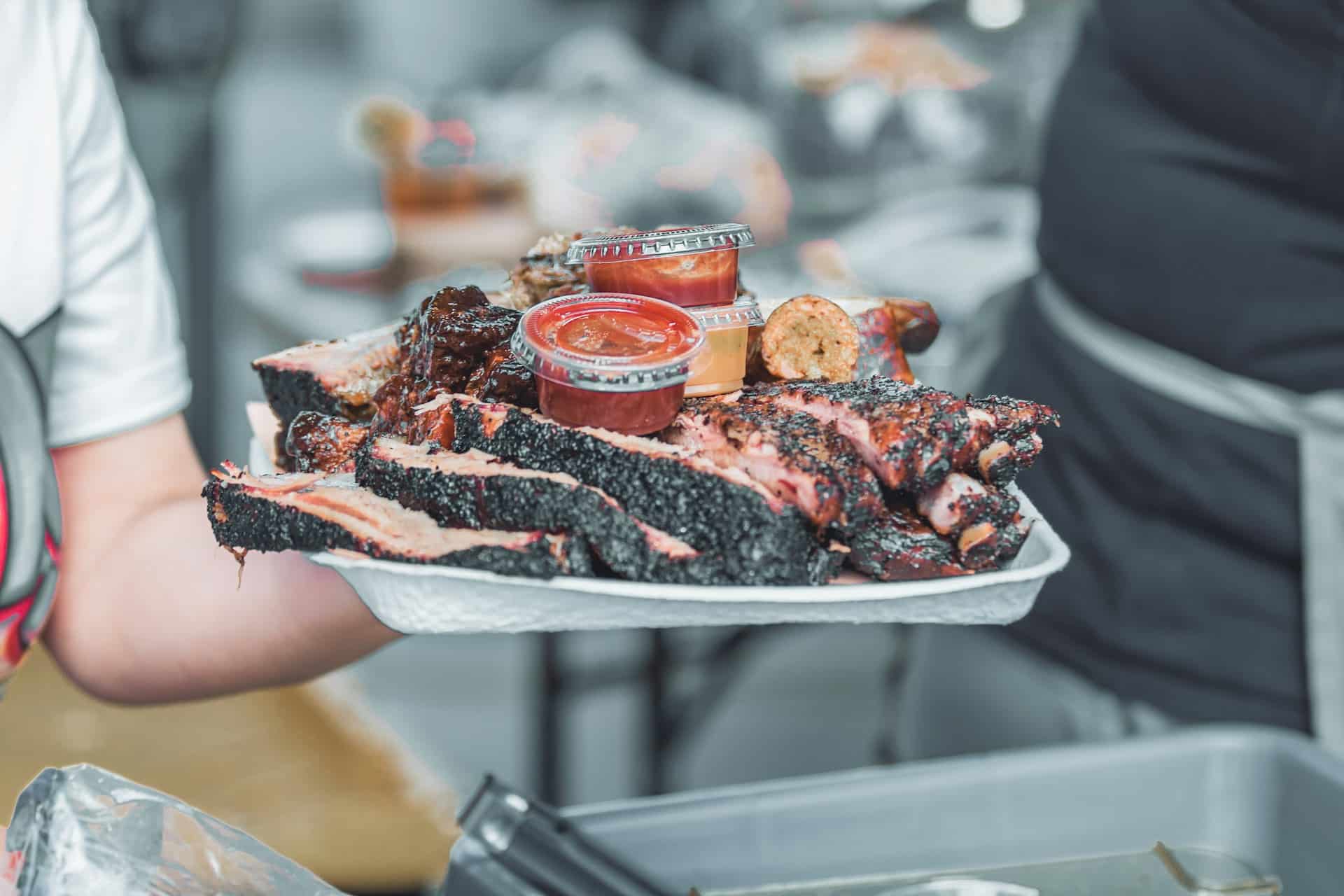Tray of smoked barbecue meats with sauce containers.