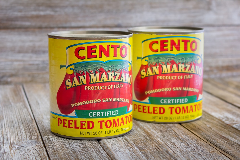 Cans of Cento San Marzano peeled tomatoes on a wooden surface.