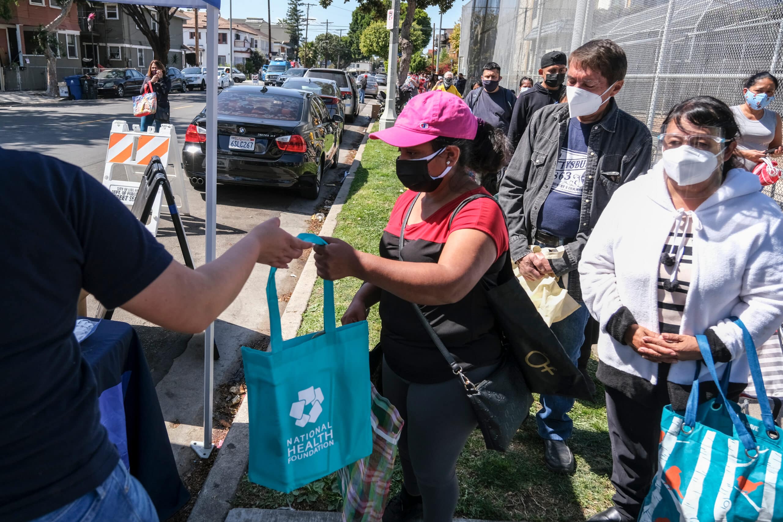 Residents line up at a community aid distribution site as volunteers hand out reusable bags during a public assistance event.