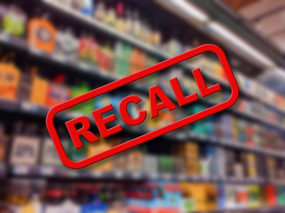 Red “recall” label over blurred grocery store shelves illustrating product recall notice.