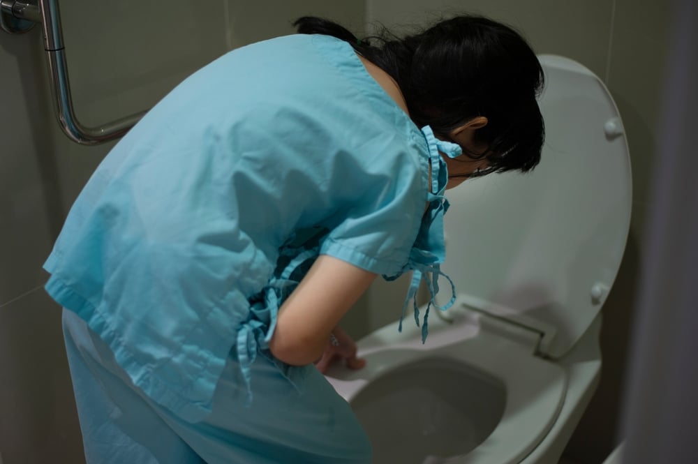 Child vomiting into a toilet in a bathroom.