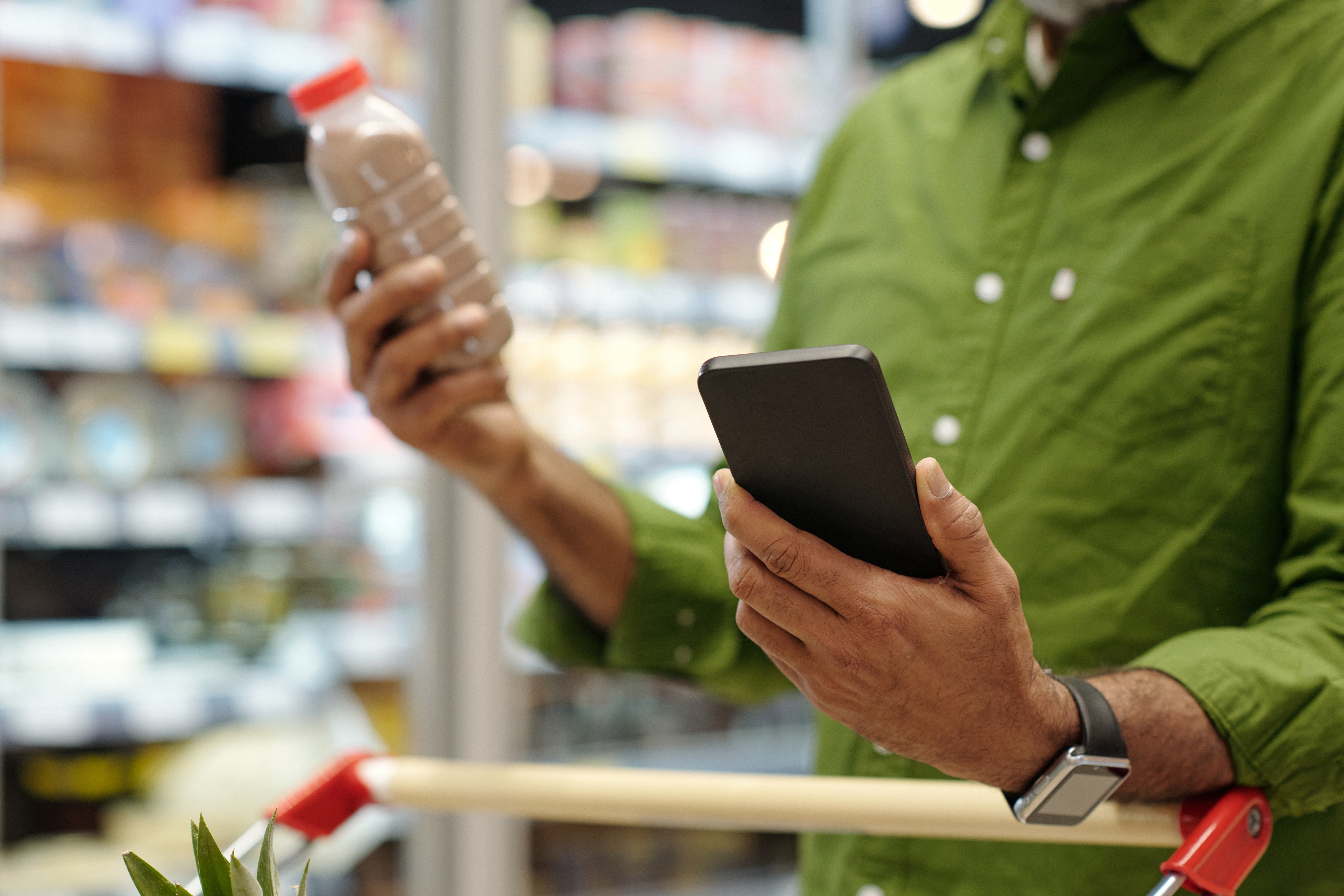 Shopper comparing a bottled chocolate milk while using a smartphone in a grocery store aisle.