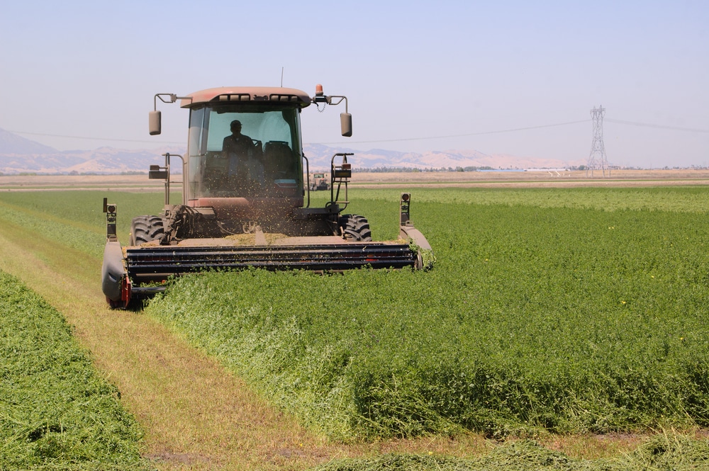 Tractor harvesting crops in a large agricultural field with mountains in the background.
